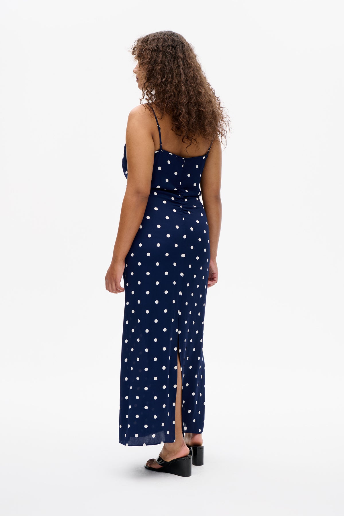 Back view of a navy spaghetti-strap maxi dress with white polka dots and a high side slit.