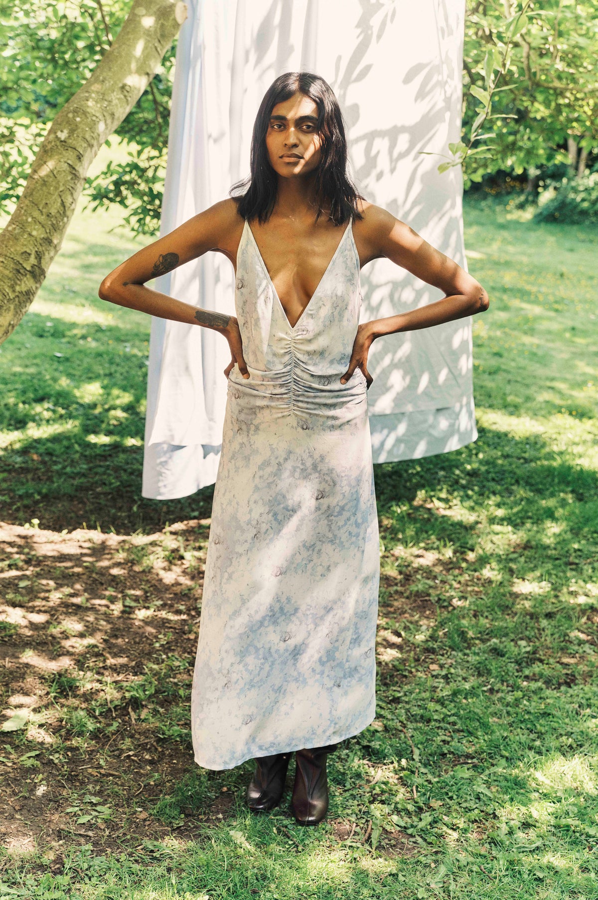 A person poses outdoors in a long ivory dress with a pale blue-grey marbled print, deep V-neck and gathered front.