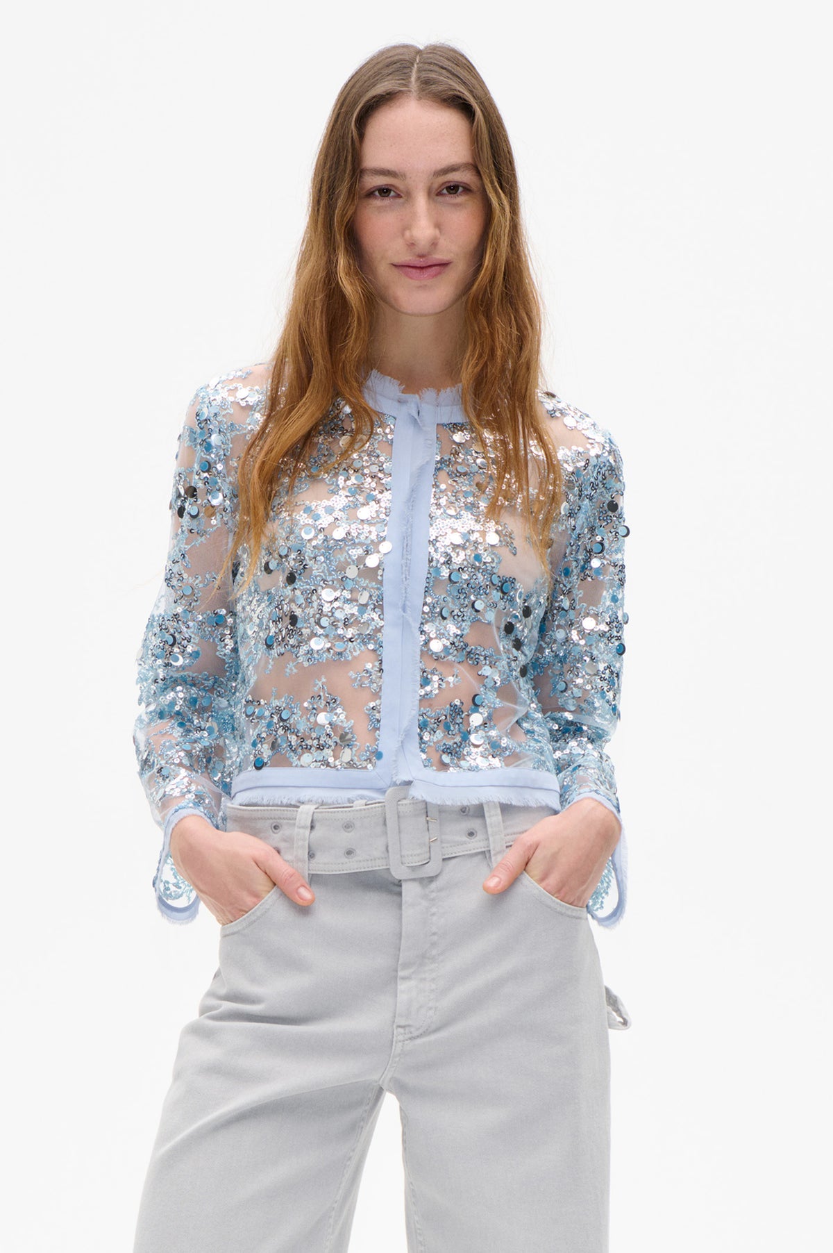 Front view of a sheer blouse covered in blue and silver sequins, with a pale blue collar and long front tie, worn with light grey jeans.