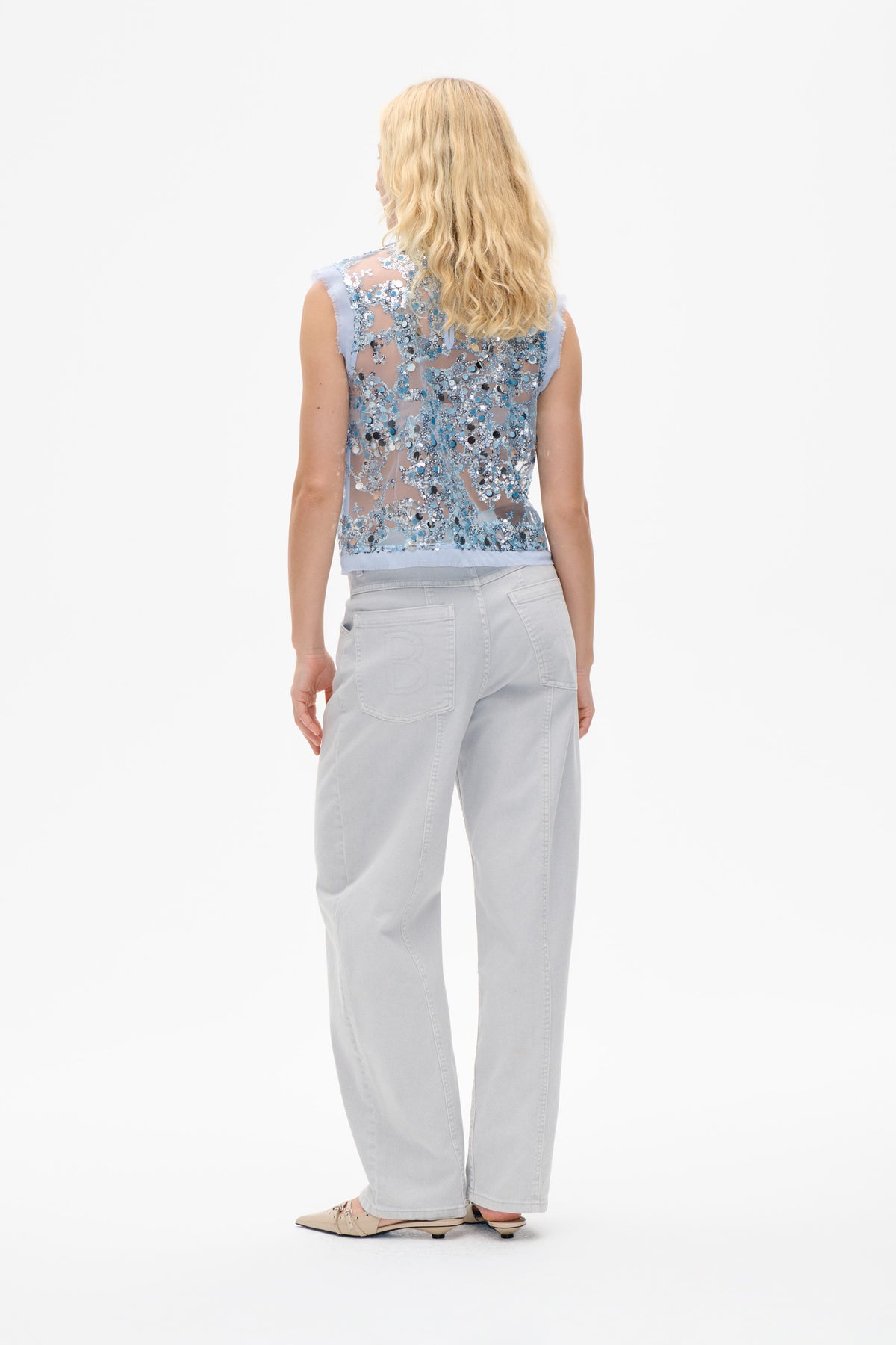 Back view of a pale blue sleeveless sheer top densely embellished with blue and silver sequins, paired with light grey jeans.