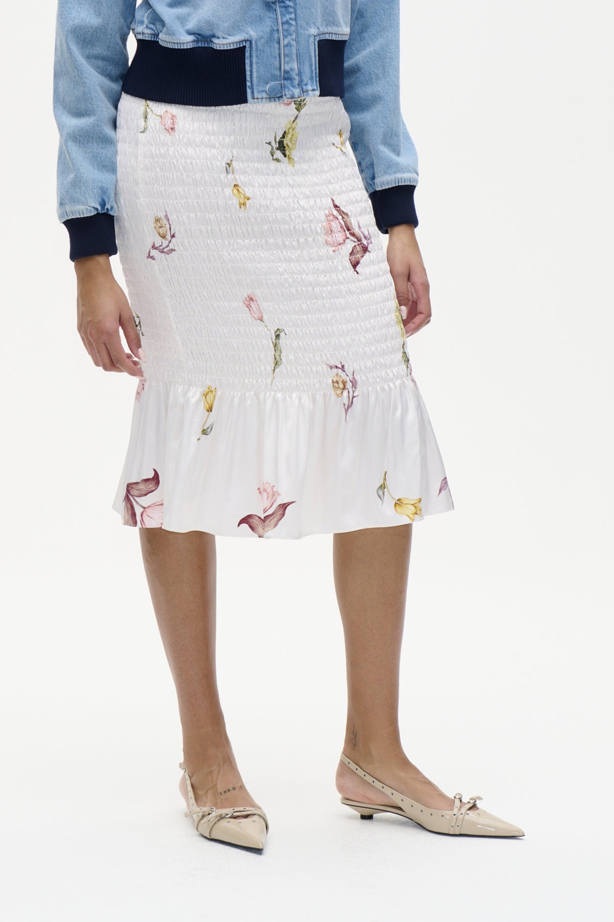Front view of a white floral-print skirt with a smocked waist, paired with a light blue denim jacket and navy knit top.