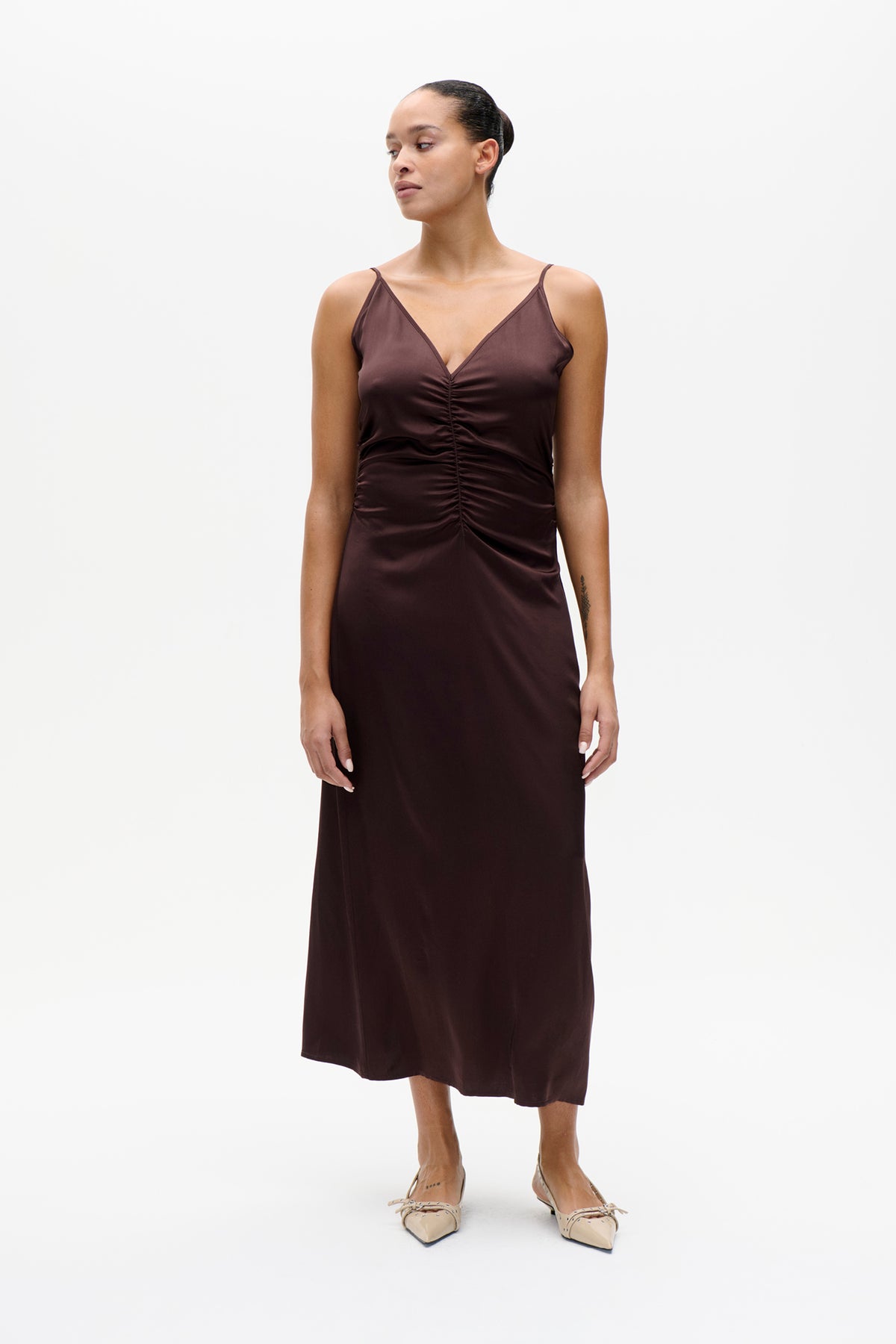Model wearing a dark brown satin midi dress with thin straps, a V-neckline and ruched front.