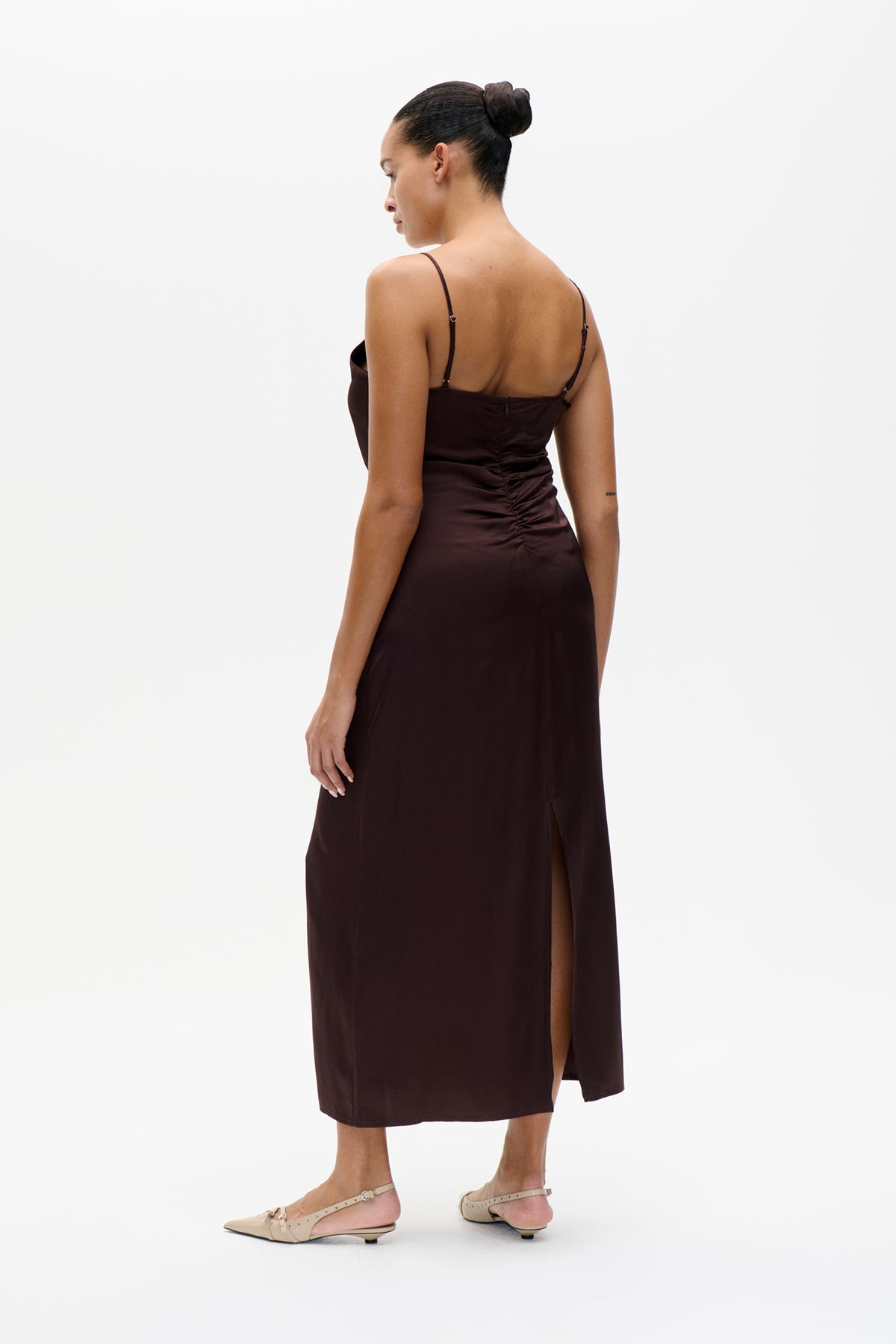 Back view of a dark brown spaghetti-strap midi dress with a ruched back, side slit and straight hem.