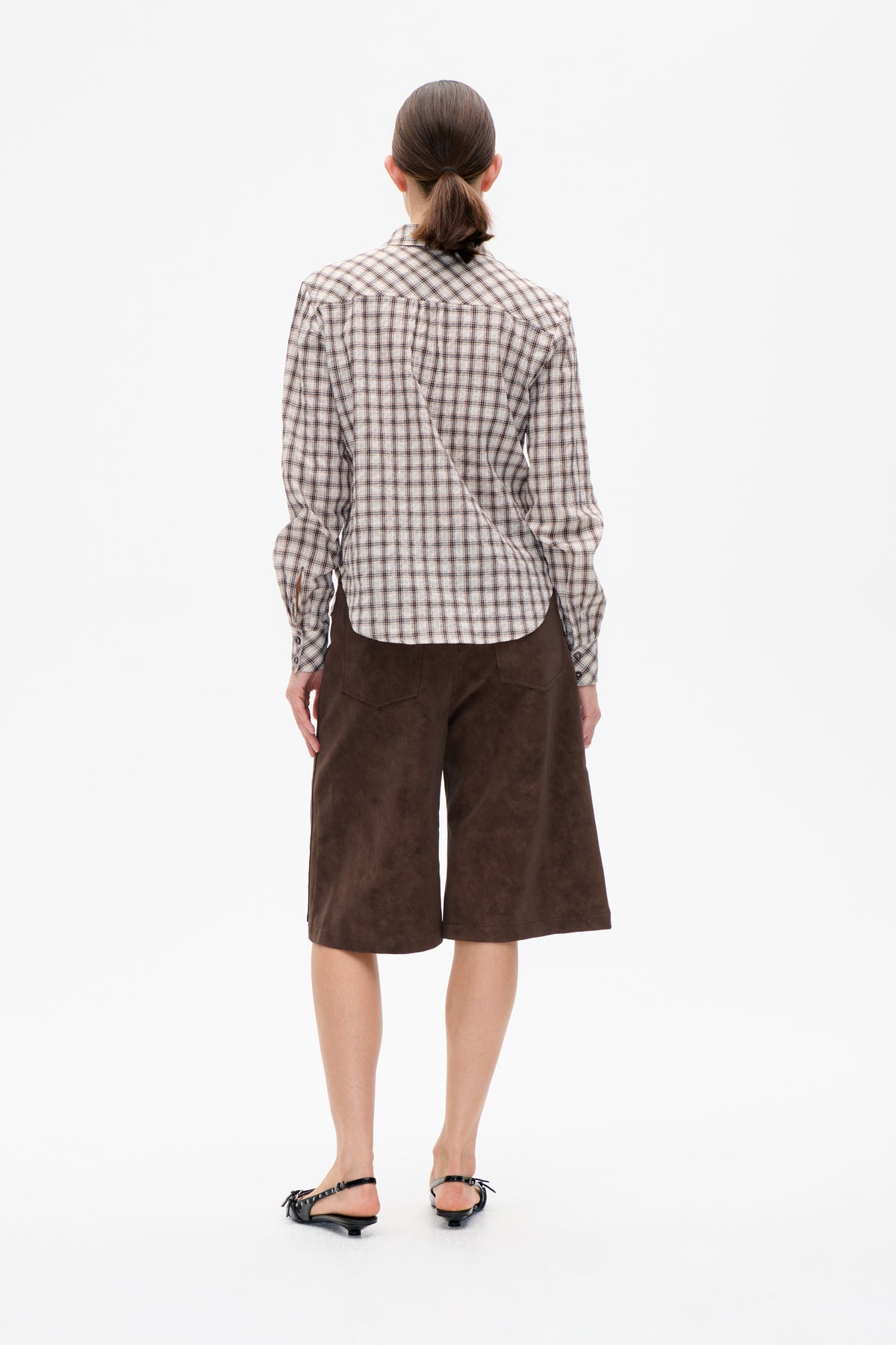 Achteraanzicht van een model met een crèmekleurige en bruine geruite blouse met lange mouwen en een donkerbruine knielange short.