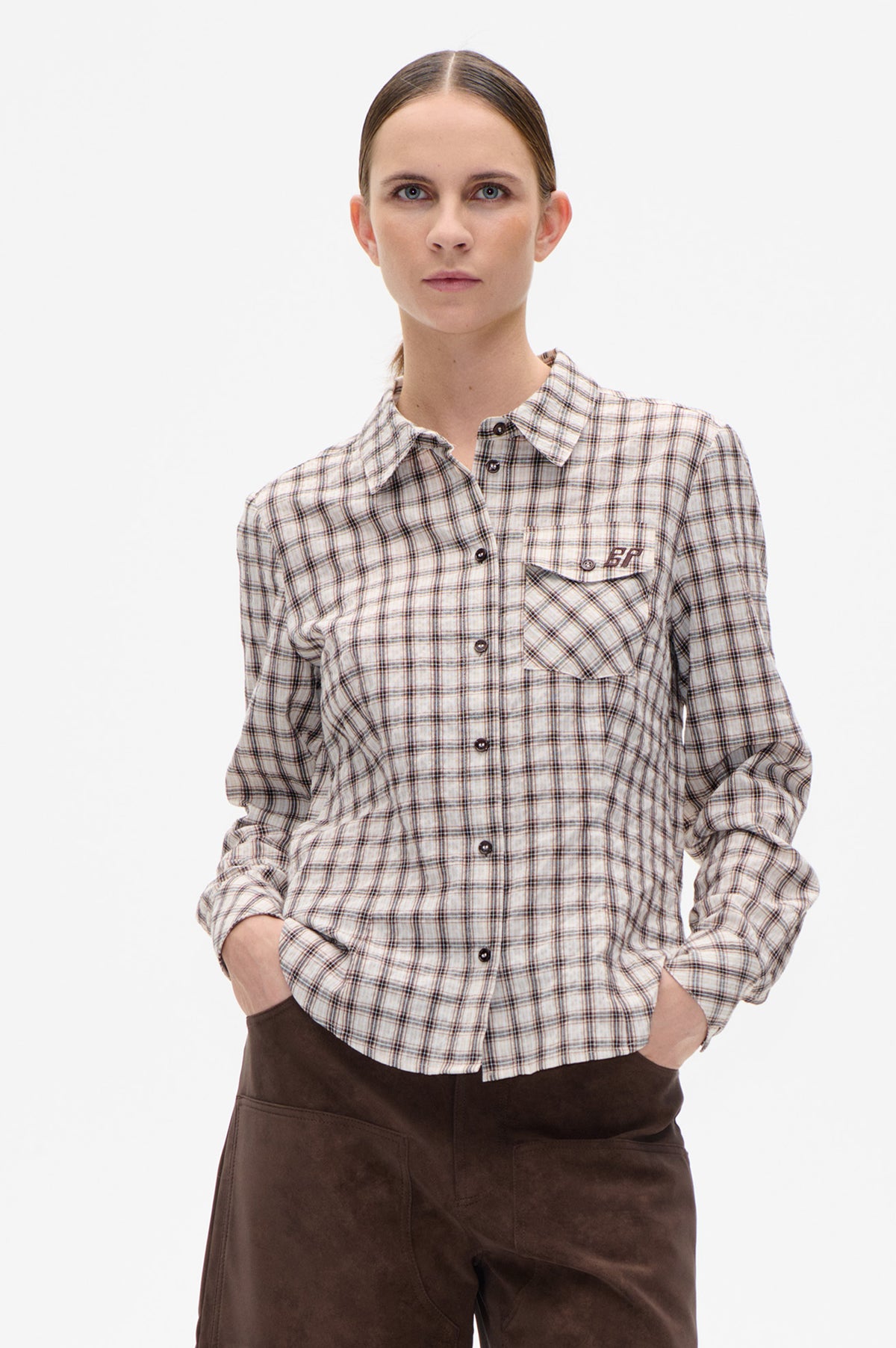 Front view of a model wearing a cream plaid button-up shirt with dark checks, chest pockets and rolled sleeves.
