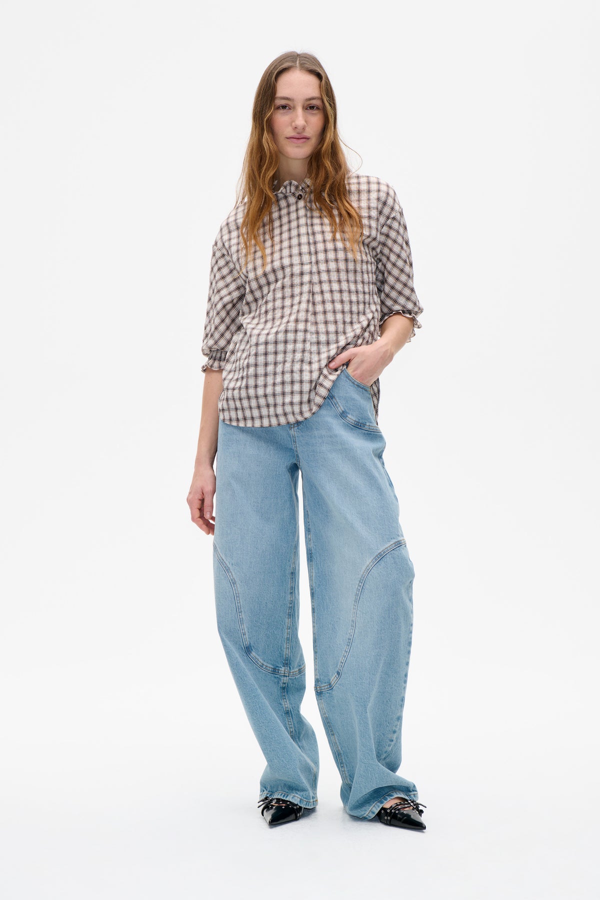 Model wearing a cream plaid blouse with a ruffled collar and cuffs, paired with light blue wide-leg jeans.