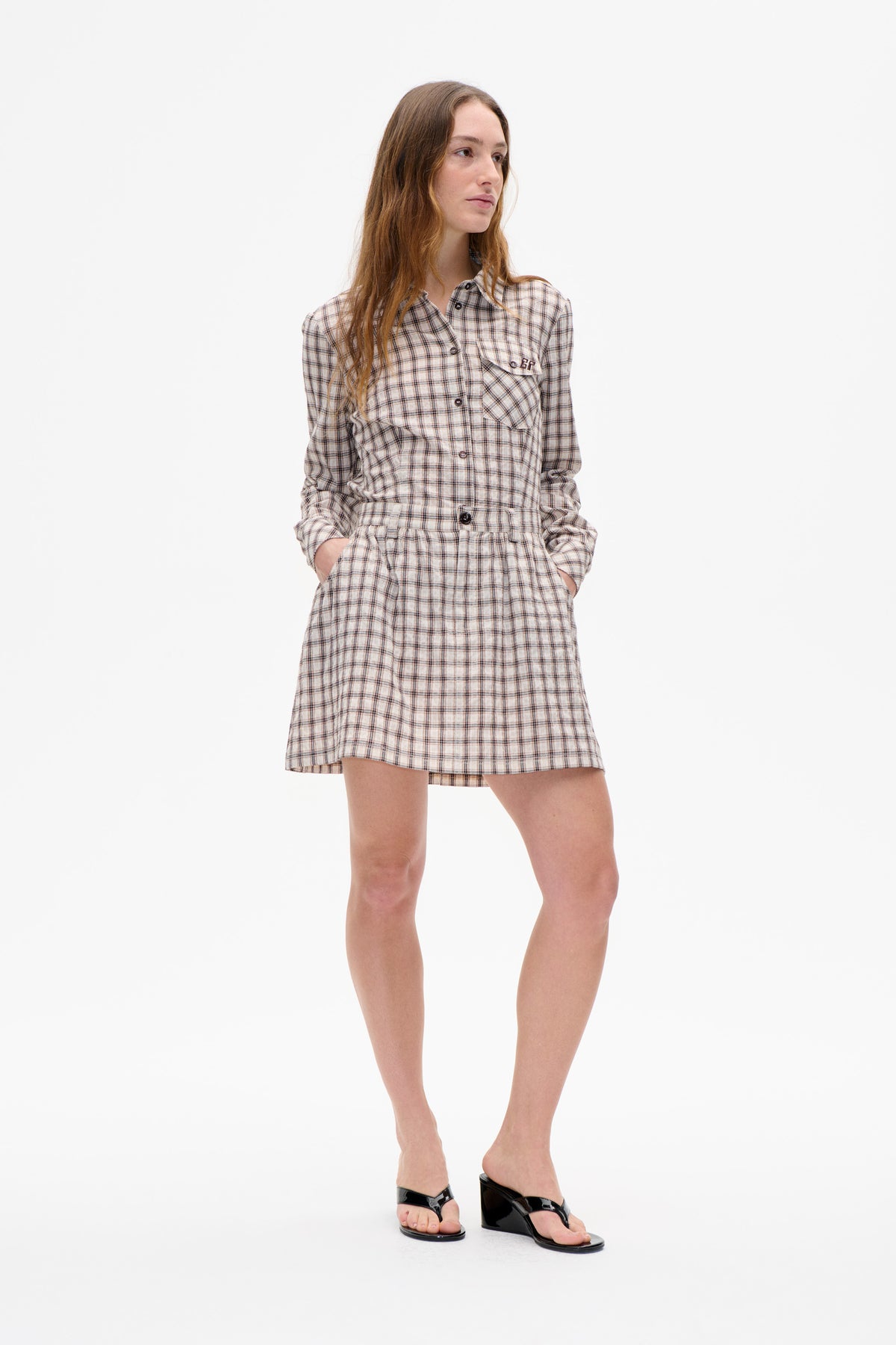 Model wearing a cream plaid button-front shirt dress with long sleeves, a gathered waist, and a flap chest pocket.