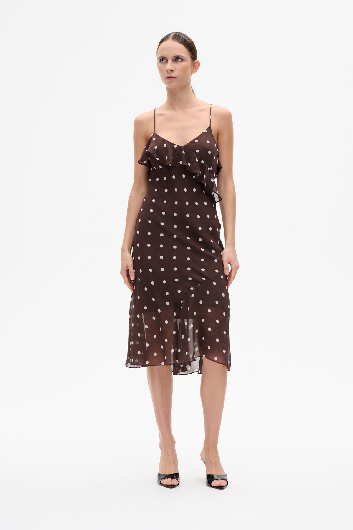 Front view of a dark brown spaghetti-strap dress with white polka dots, a V-neckline and layered ruffle detail across the bodice.