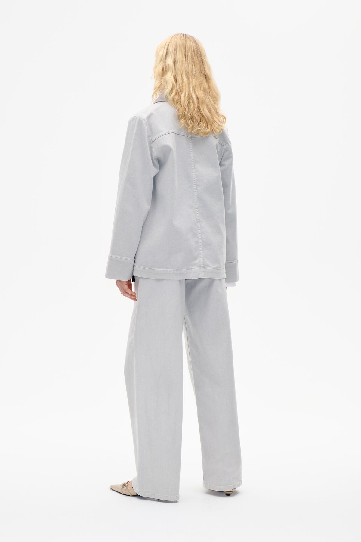 Back view of a model wearing a pale grey jacket with seam details and matching wide-leg trousers.