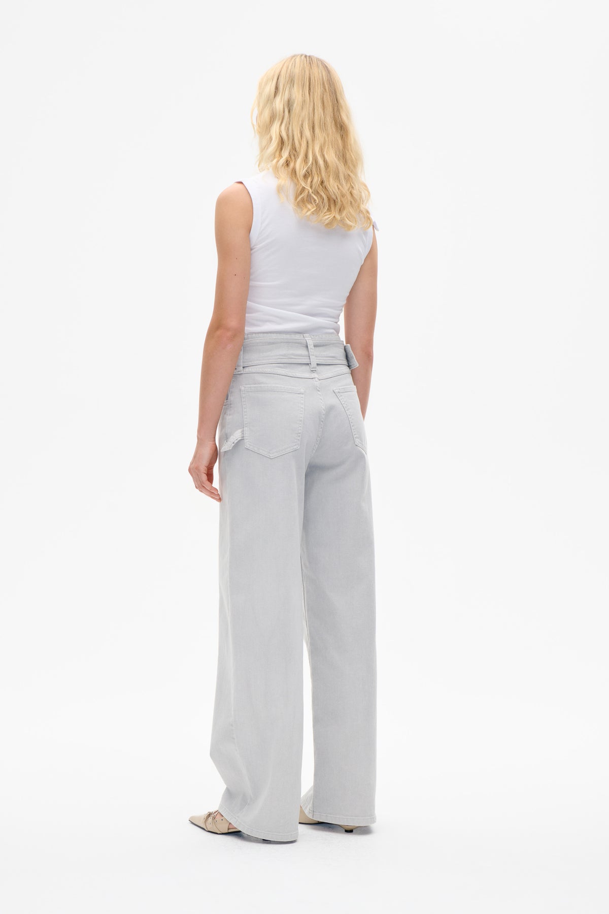 Back view of a model wearing pale grey wide-leg jeans with belt loops and patch pockets, paired with a white sleeveless top.