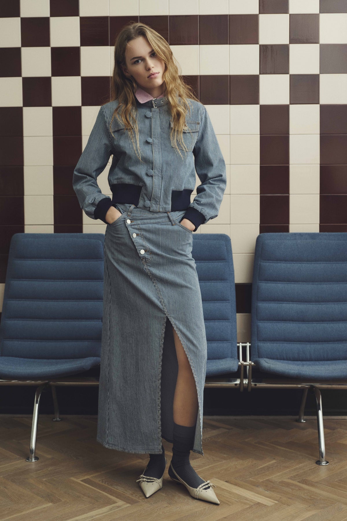Model wearing a blue-and-white pinstripe jacket with pink collar and matching button-front skirt with a high slit