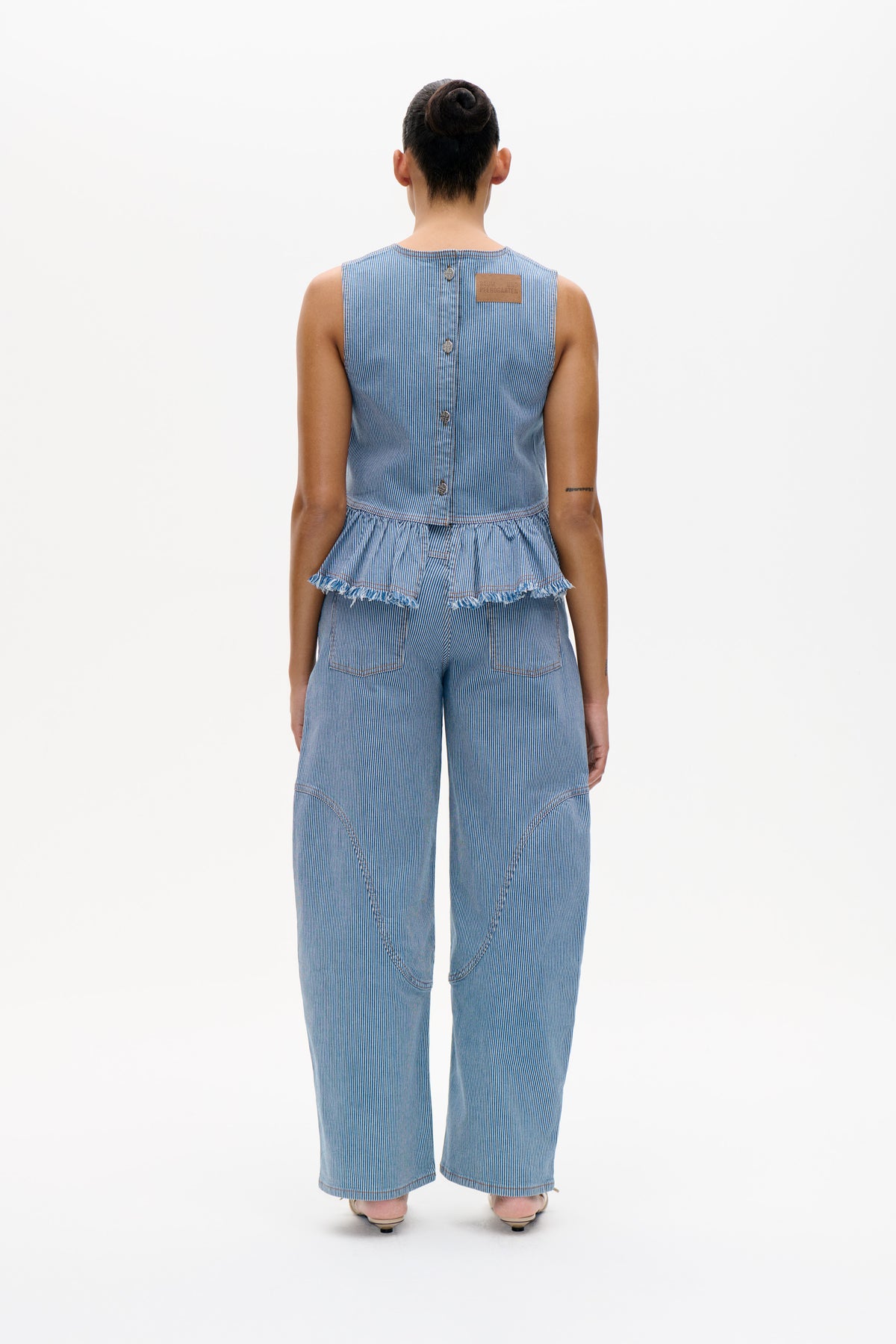 Rear view of a model wearing a blue-and-white pinstripe sleeveless peplum top with matching wide-leg trousers.