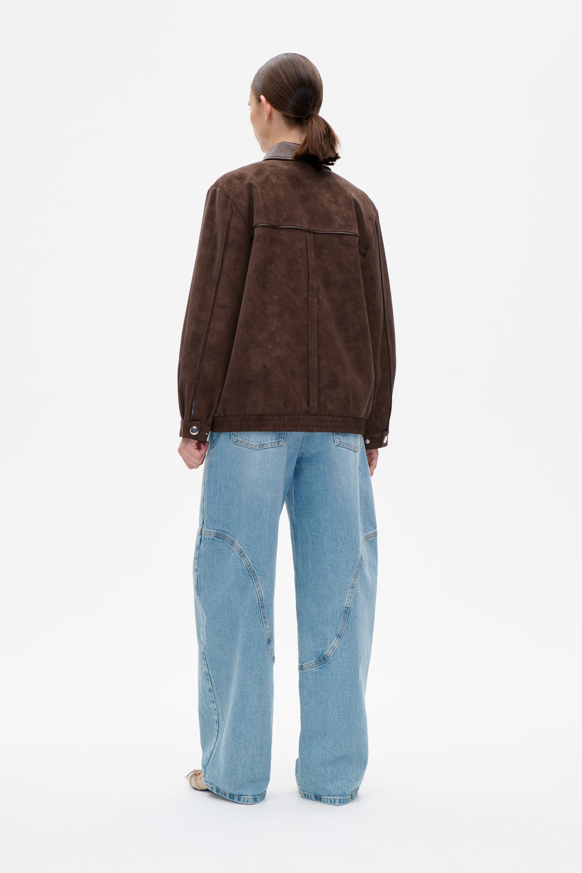Vue de dos d'un mannequin portant une veste chinée marron foncé à col pointu, avec empiècement au dos et poignets à pression, associée à un jean bleu clair.