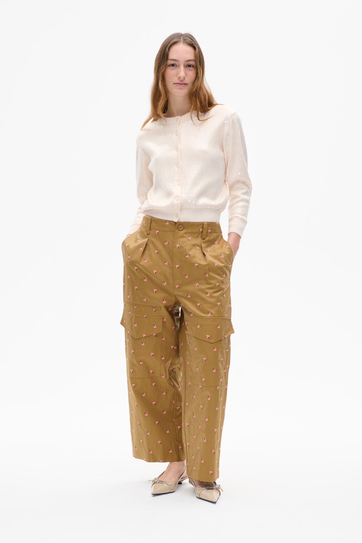 Model wearing an ivory sequined button-front cardigan and tan wide-leg trousers with small pink flowers and cargo pockets.