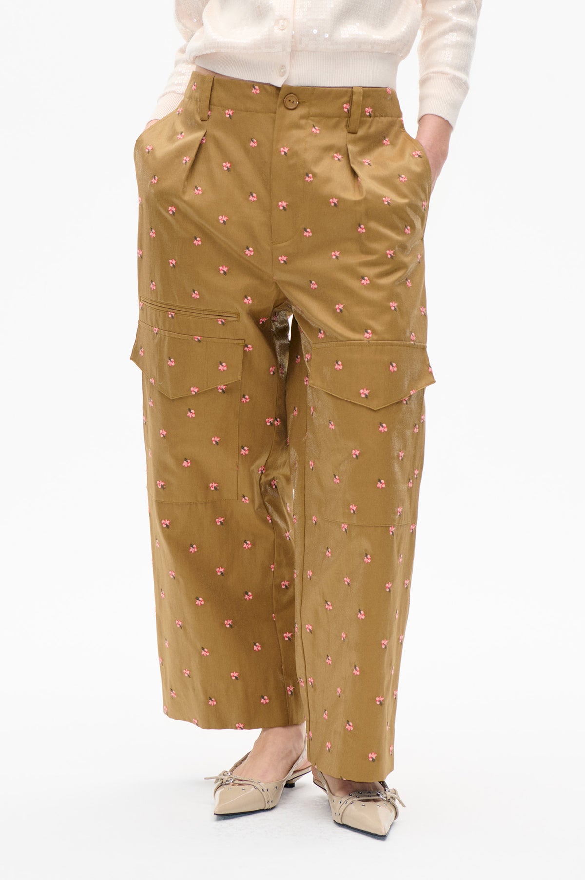 Front view of ochre-brown wide-leg trousers with scattered pink floral print, button fastening and large patch pockets, styled with a cream cardigan.