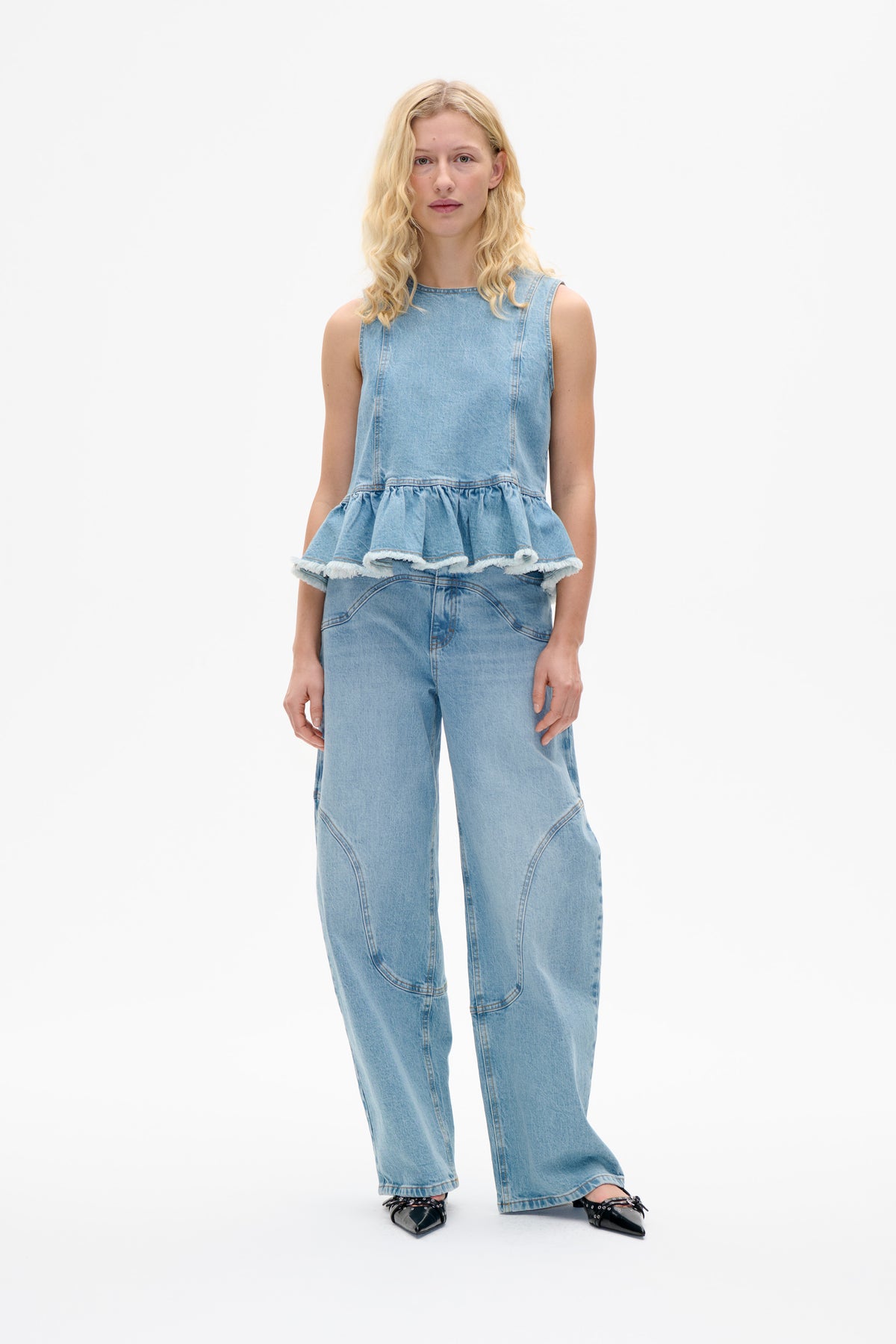 Model wearing a light-wash sleeveless denim top with a gathered, frayed peplum hem and matching wide-leg jeans, front view.