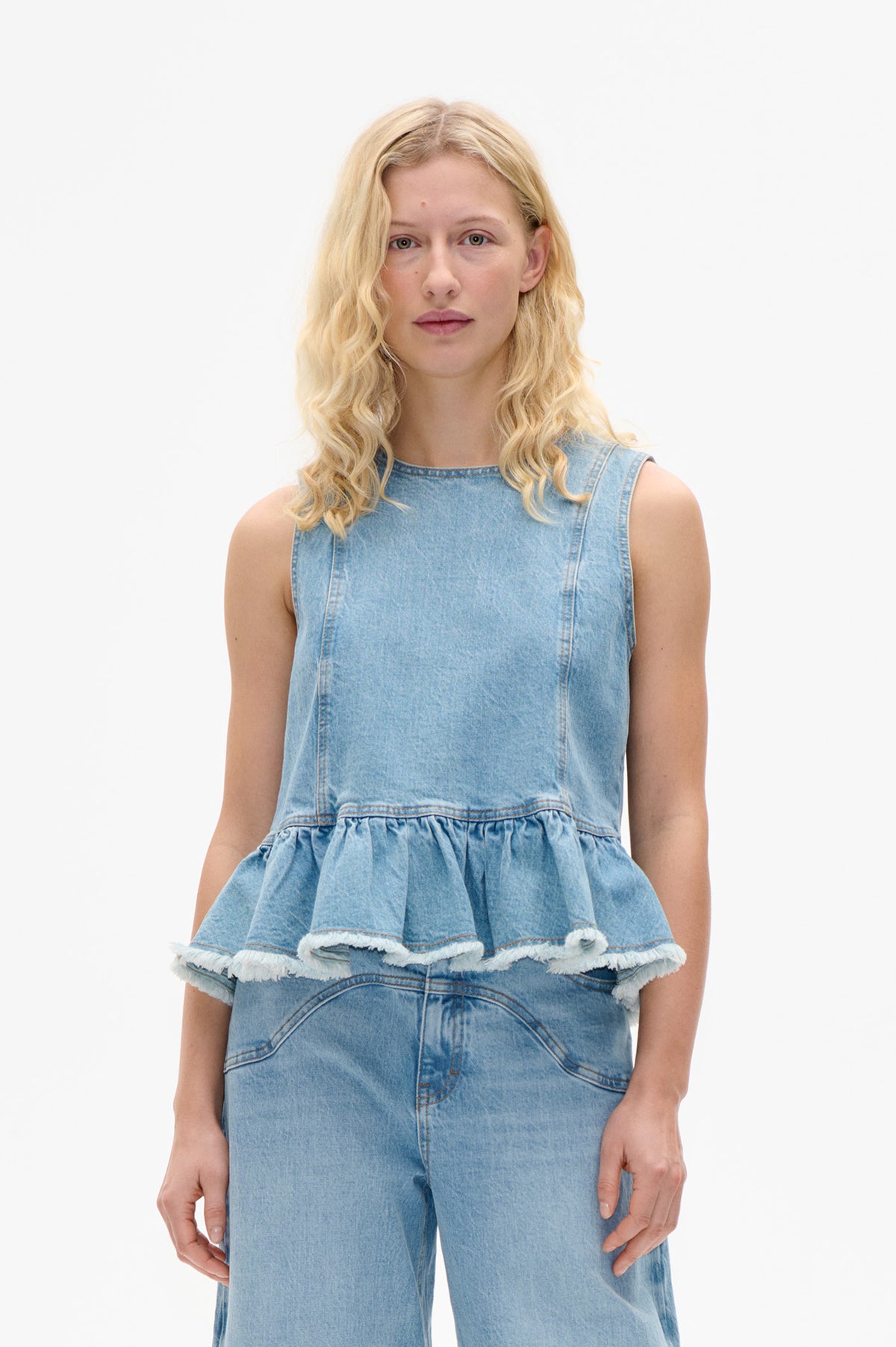 Front view of a light blue sleeveless denim top with a high neckline and gathered peplum hem with frayed edges.