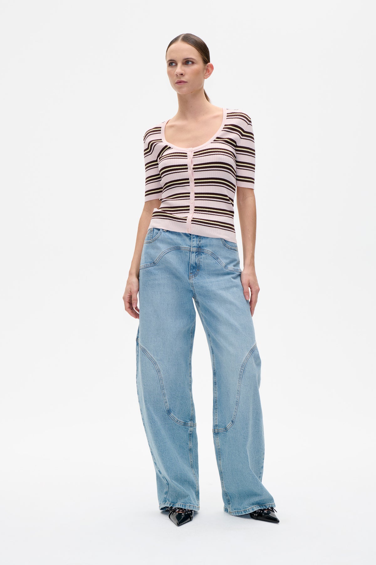 Front view of a model wearing a pale pink ribbed button-front top with dark horizontal stripes and light blue wide-leg jeans.
