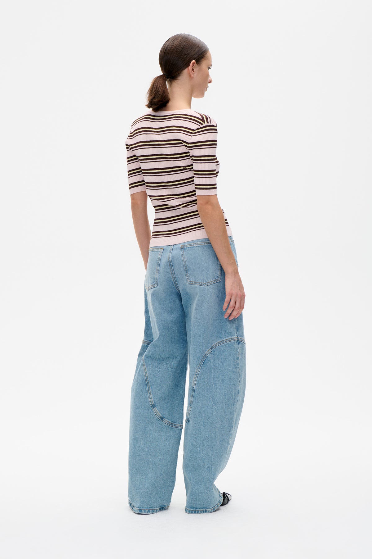 Back view of a pale pink ribbed short-sleeve top with dark brown and cream horizontal stripes, styled with wide-leg light blue jeans.