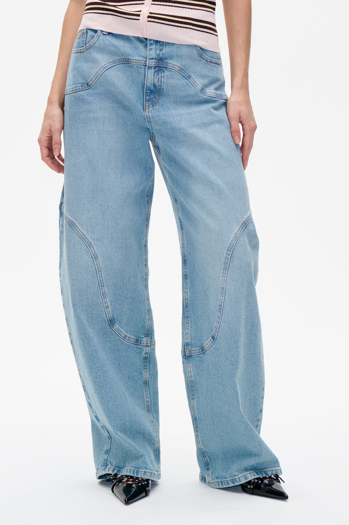 Front detail of light-wash blue wide-leg jeans with curved seam panels, worn with a pale pink striped cardigan.