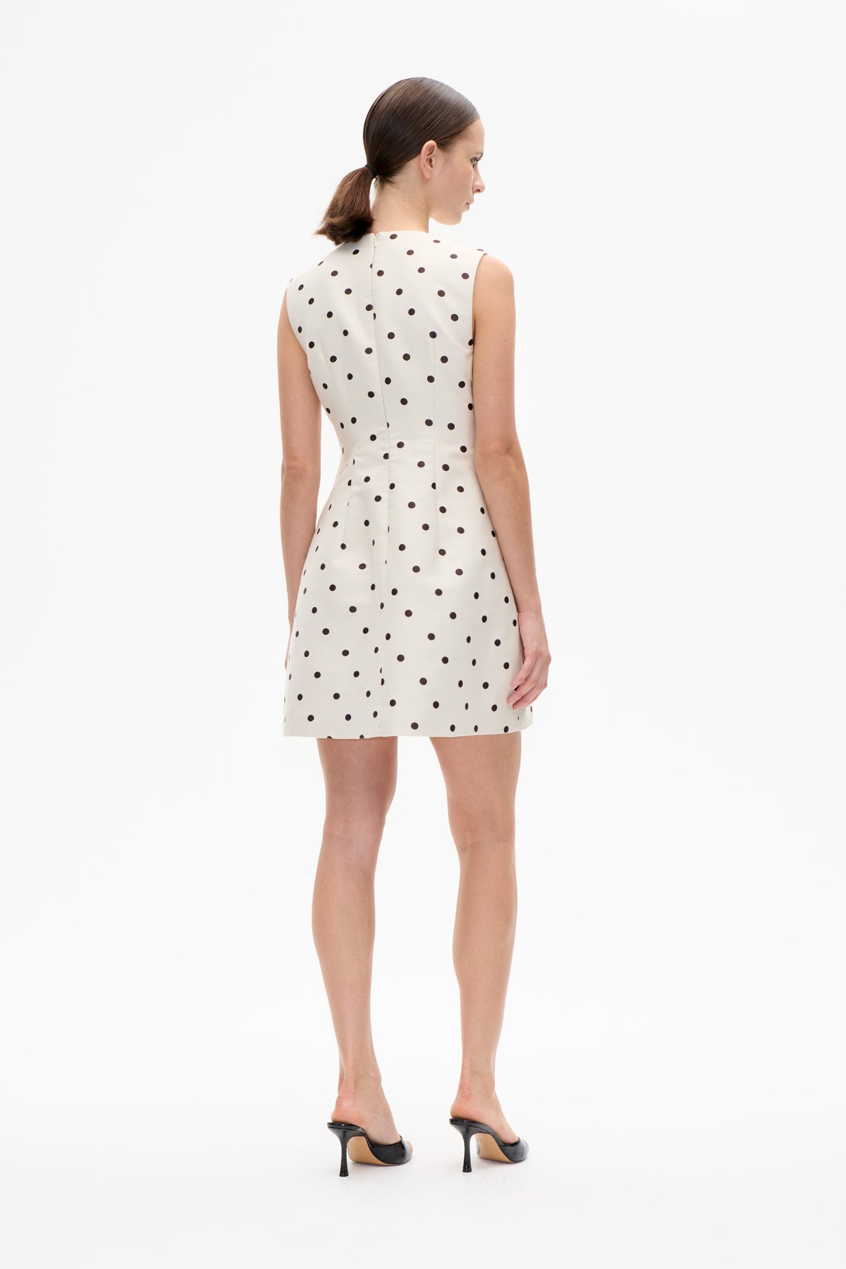 Back view of a sleeveless cream mini dress with black polka dots and a centre-back fastening.