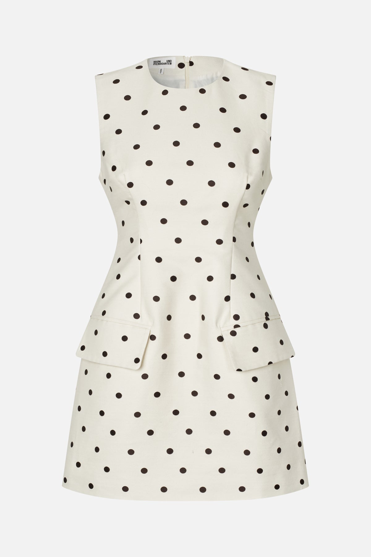 Front view of a sleeveless cream dress with black polka dots, a round neckline, fitted waist and flared skirt with flap pockets.