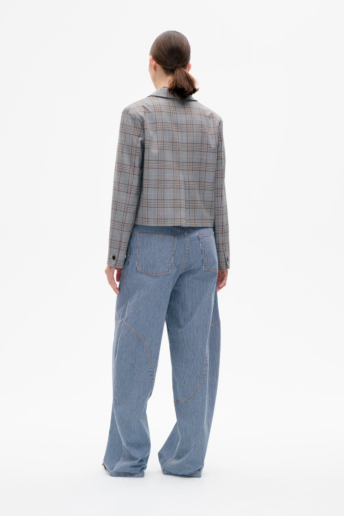 Back view of a model wearing a grey plaid blazer with blue-and-white pinstriped wide-leg trousers.