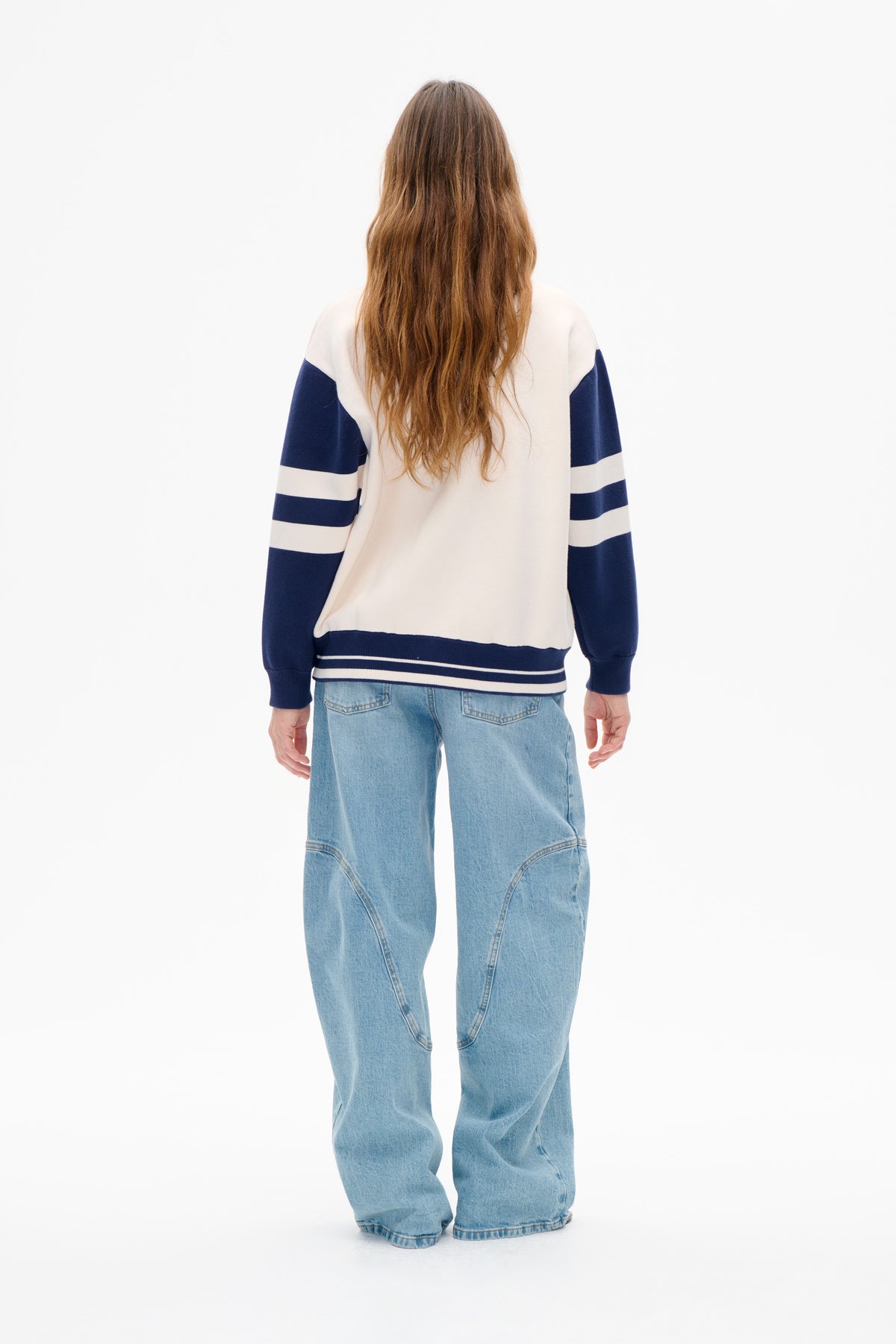 Vue de dos d'un sweat-shirt crème à rayures horizontales bleu marine sur les manches, avec poignets et ourlet côtelés, porté avec un jean bleu clair.