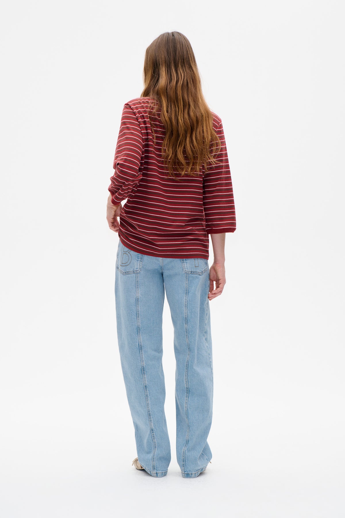 Rückenansicht eines Models, das ein rotes Langarmtop mit dünnen weißen und dunklen Querstreifen und eine helle Jeans trägt.