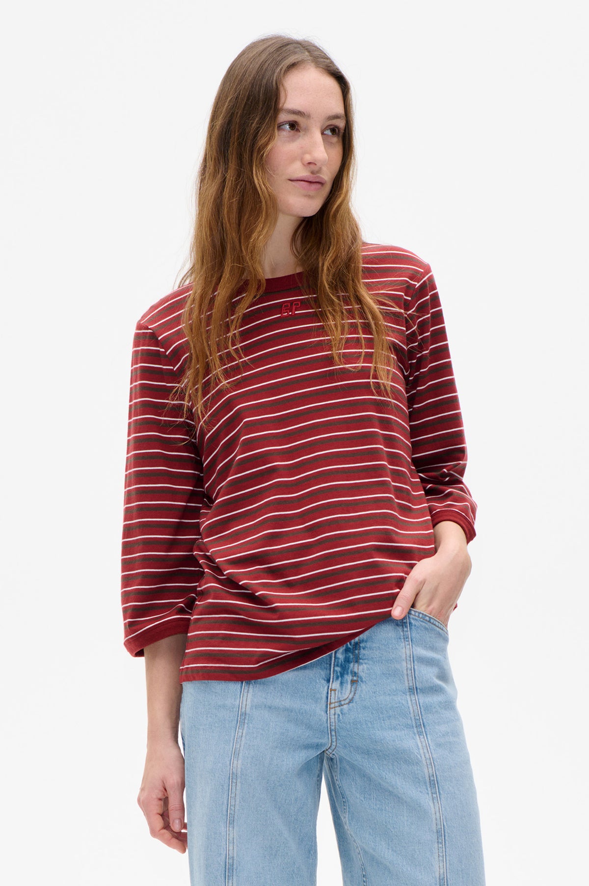 Model wearing a red long-sleeve crew-neck top with white and dark horizontal stripes and light-wash jeans, shown from the front.
