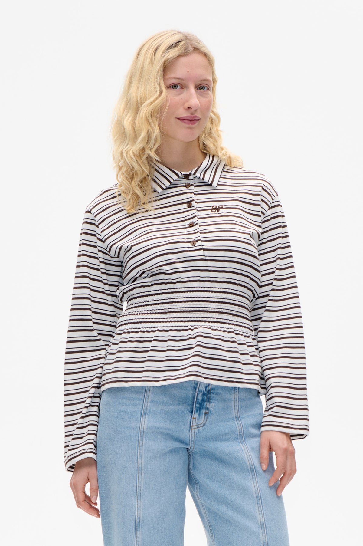 Front view of a white long-sleeved button-up shirt with dark horizontal stripes and a gathered waist, paired with light blue jeans.
