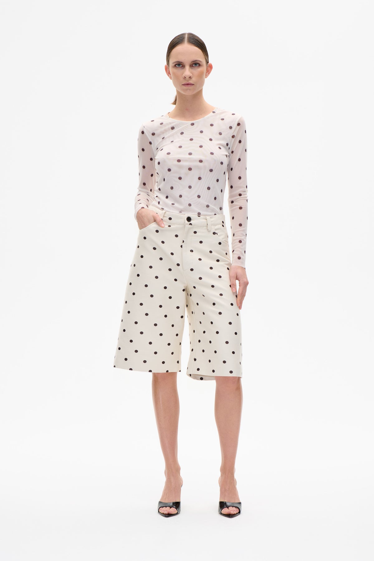 Front-facing model wearing a white long-sleeved top with dark polka dots and matching wide-leg shorts against a white background.