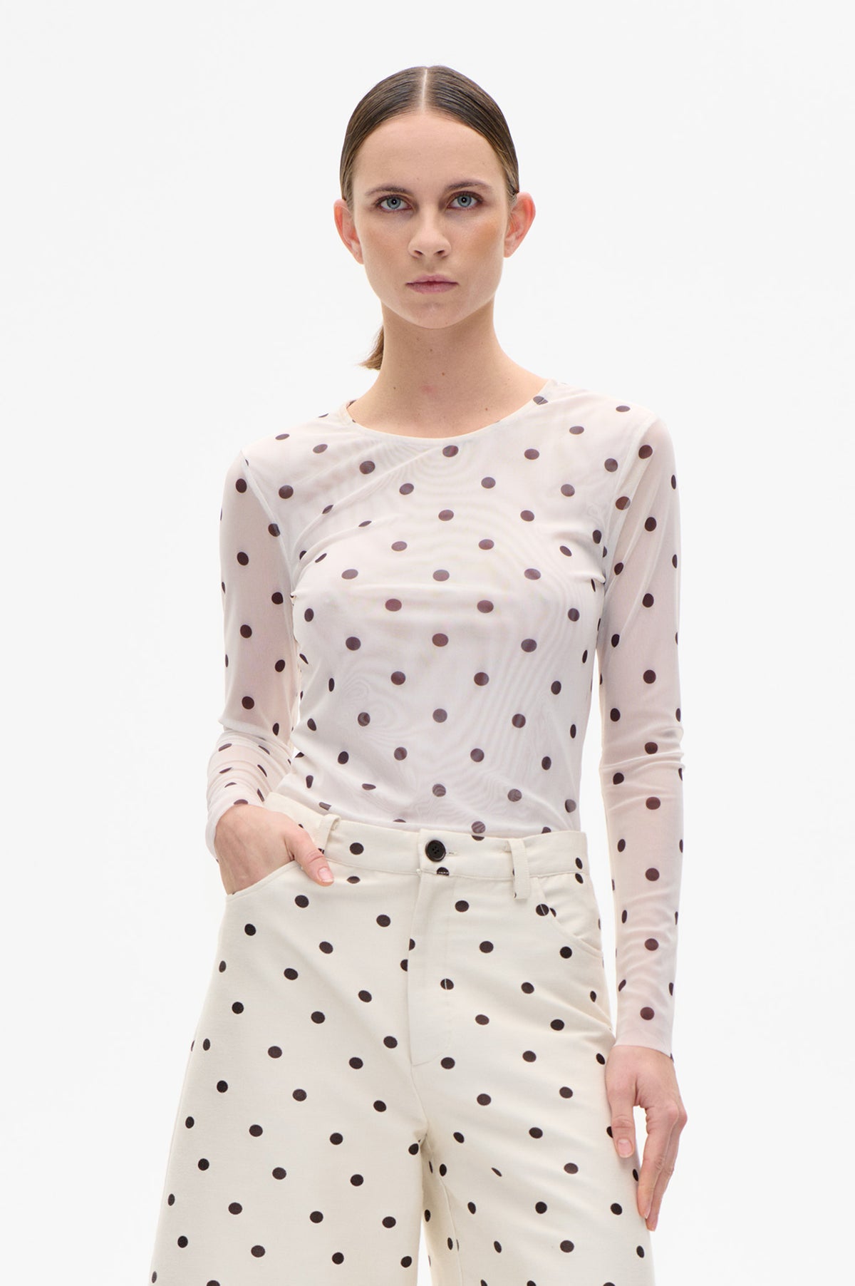 Front view of a model wearing a cream long-sleeve top and matching trousers with dark polka dots.