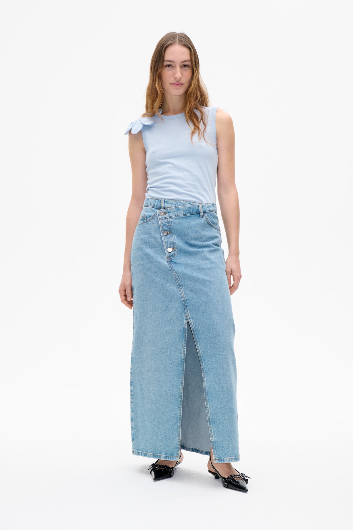 Front view of a model wearing a pale blue sleeveless top with a shoulder bow and a light-wash denim maxi skirt with front buttons and a slit.