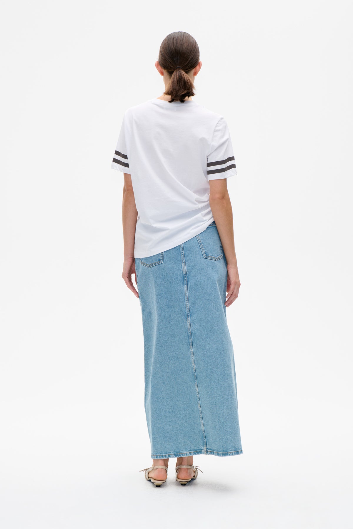 Back view of a white short-sleeved T-shirt with dark sleeve stripes, paired with a light blue denim midi skirt.