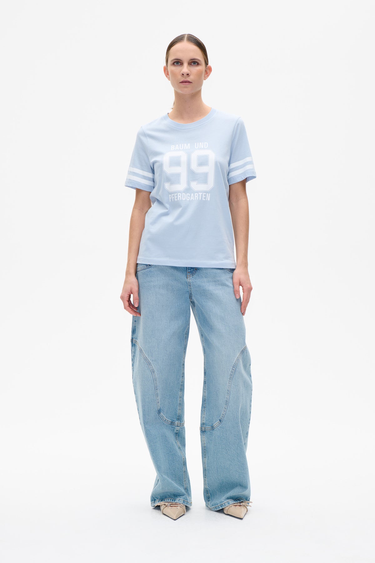 Front view of a pale blue short-sleeved T-shirt with white Baum und Pferdgarten 99 lettering and striped sleeves.