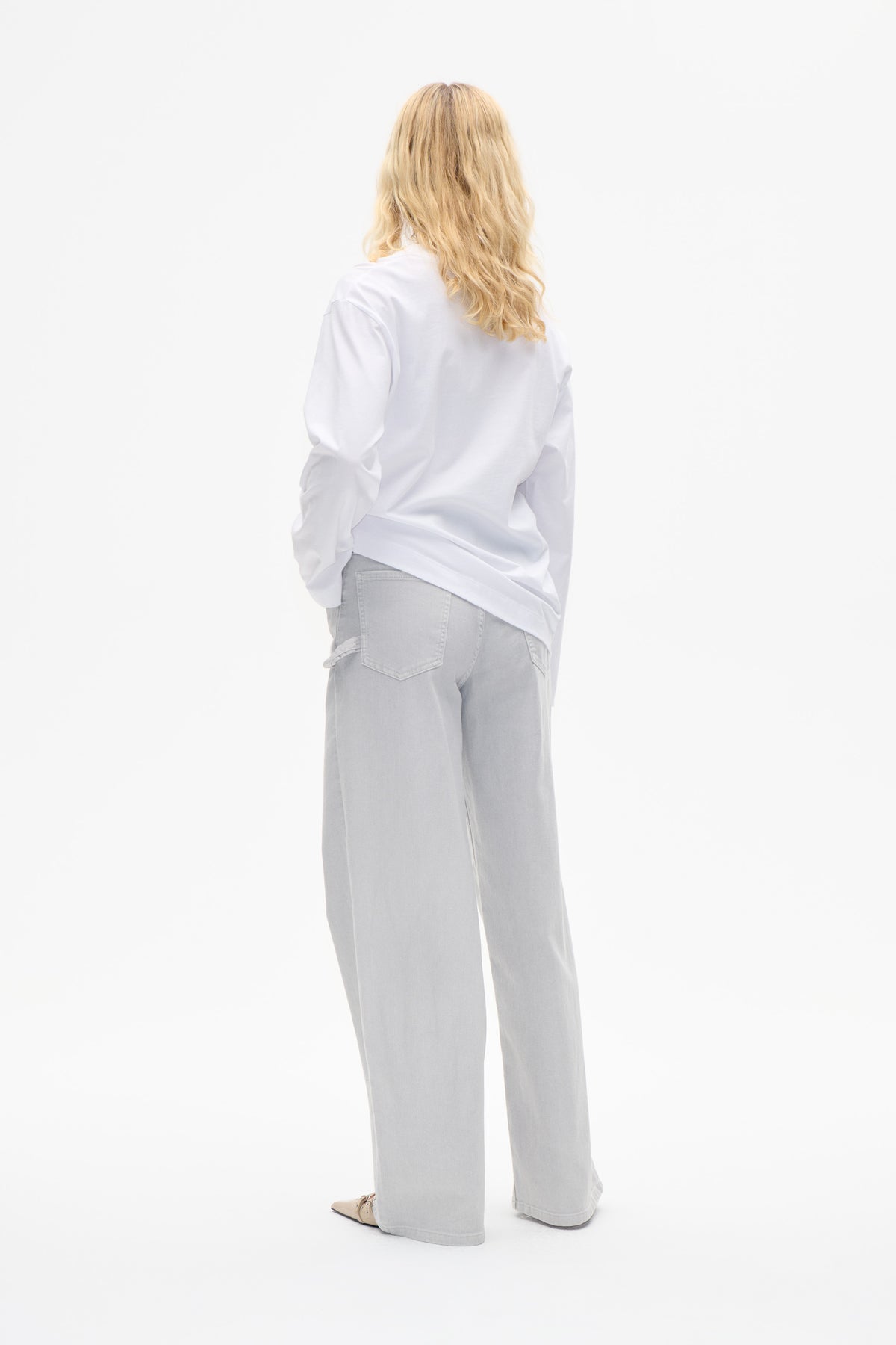 Rückenansicht eines Models, das ein weites weißes Langarmshirt und hellgraue, weit geschnittene Jeans trägt.
