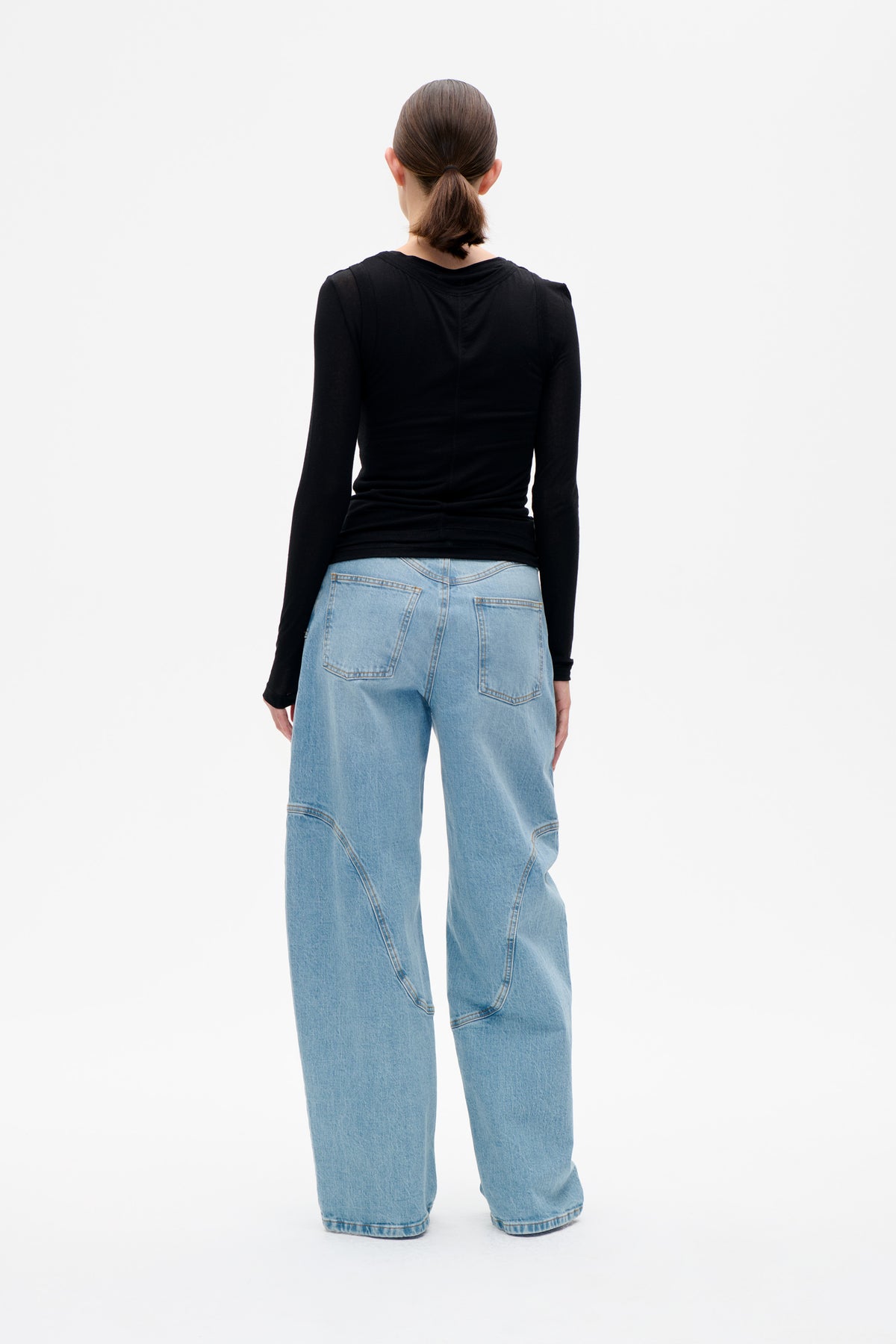 Back view of a model wearing a fitted black long-sleeved top and wide-leg light-wash jeans with curved seam details.