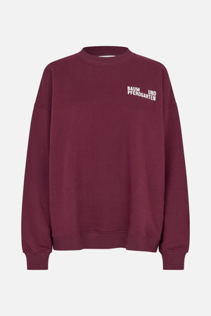 Vooraanzicht van een bordeauxrood sweatshirt met ronde hals, geribde manchetten en boord, en witte Baum und Pferdgarten-letters op de borst.