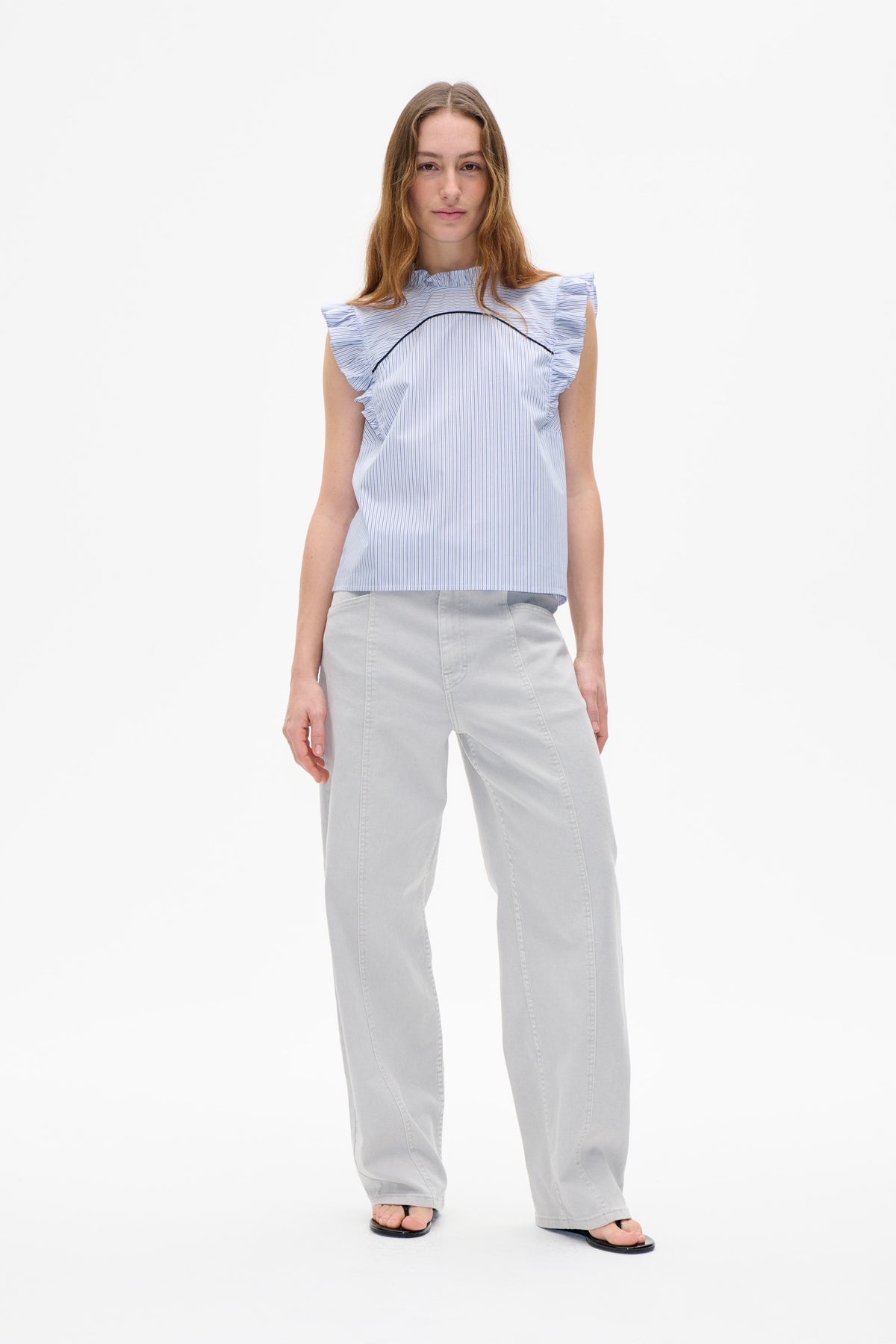 Front view of a white blouse with fine blue stripes, ruffled cap sleeves and neckline, and black curved piping across the chest.