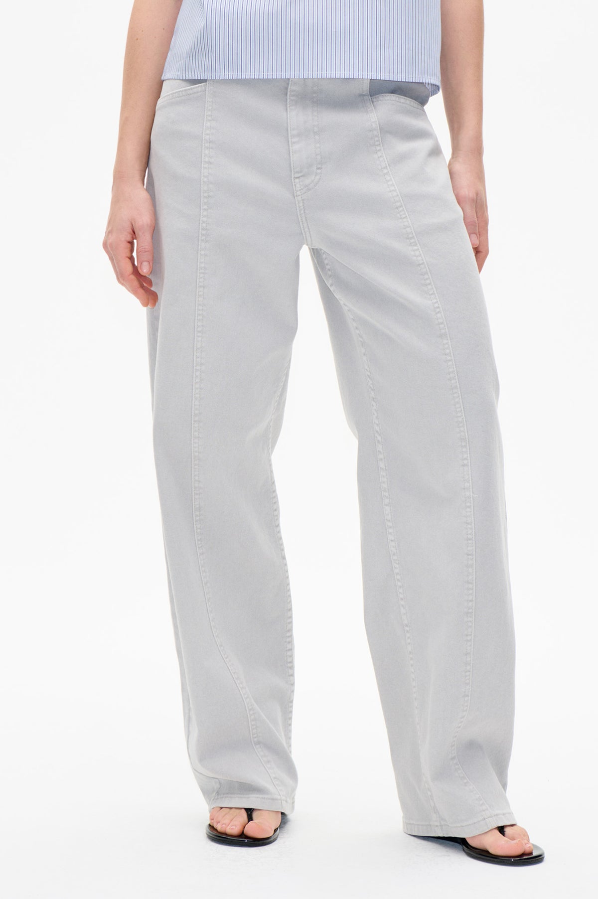 Front detail of pale grey wide-leg jeans with curved panel seams and front pockets, worn with a blue-and-white striped top.