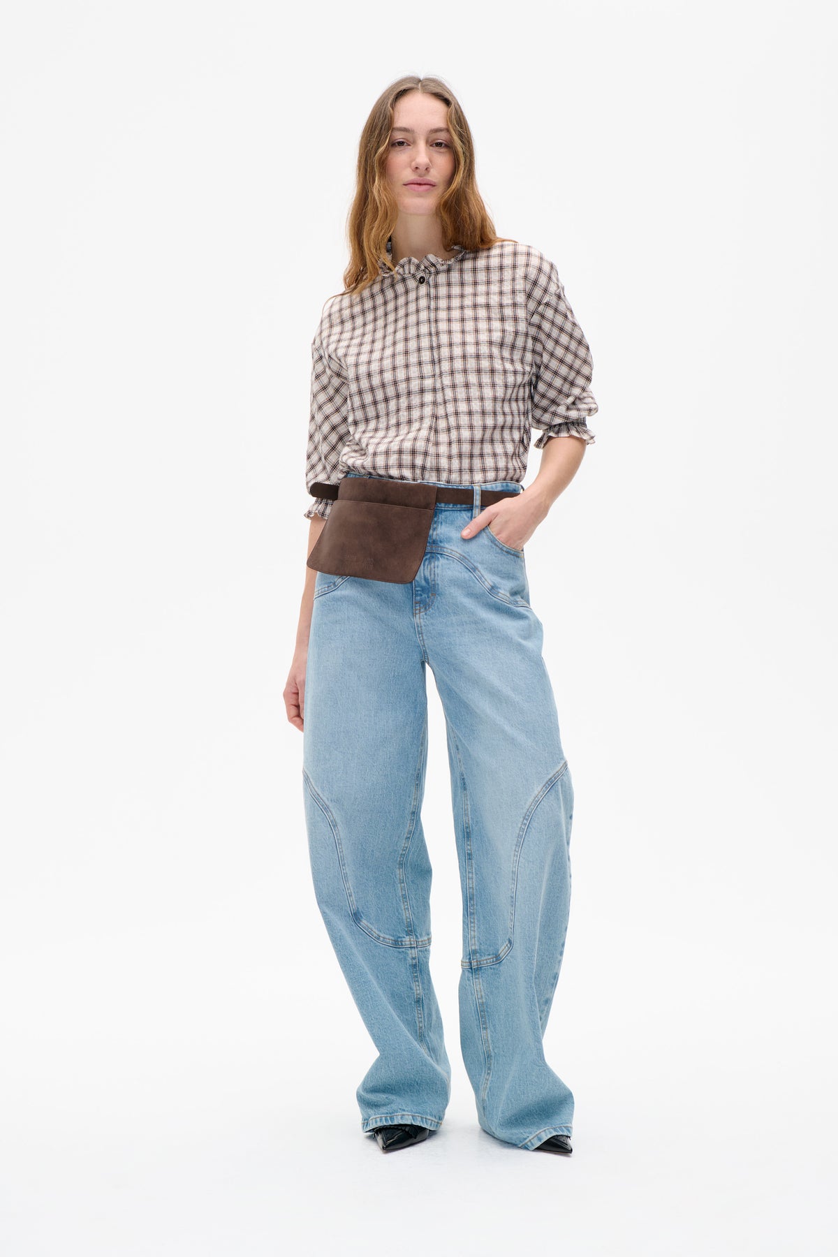 Model wearing a cream plaid button-front blouse with a ruffled collar and cuffs, light-wash wide-leg jeans and a brown waist bag.