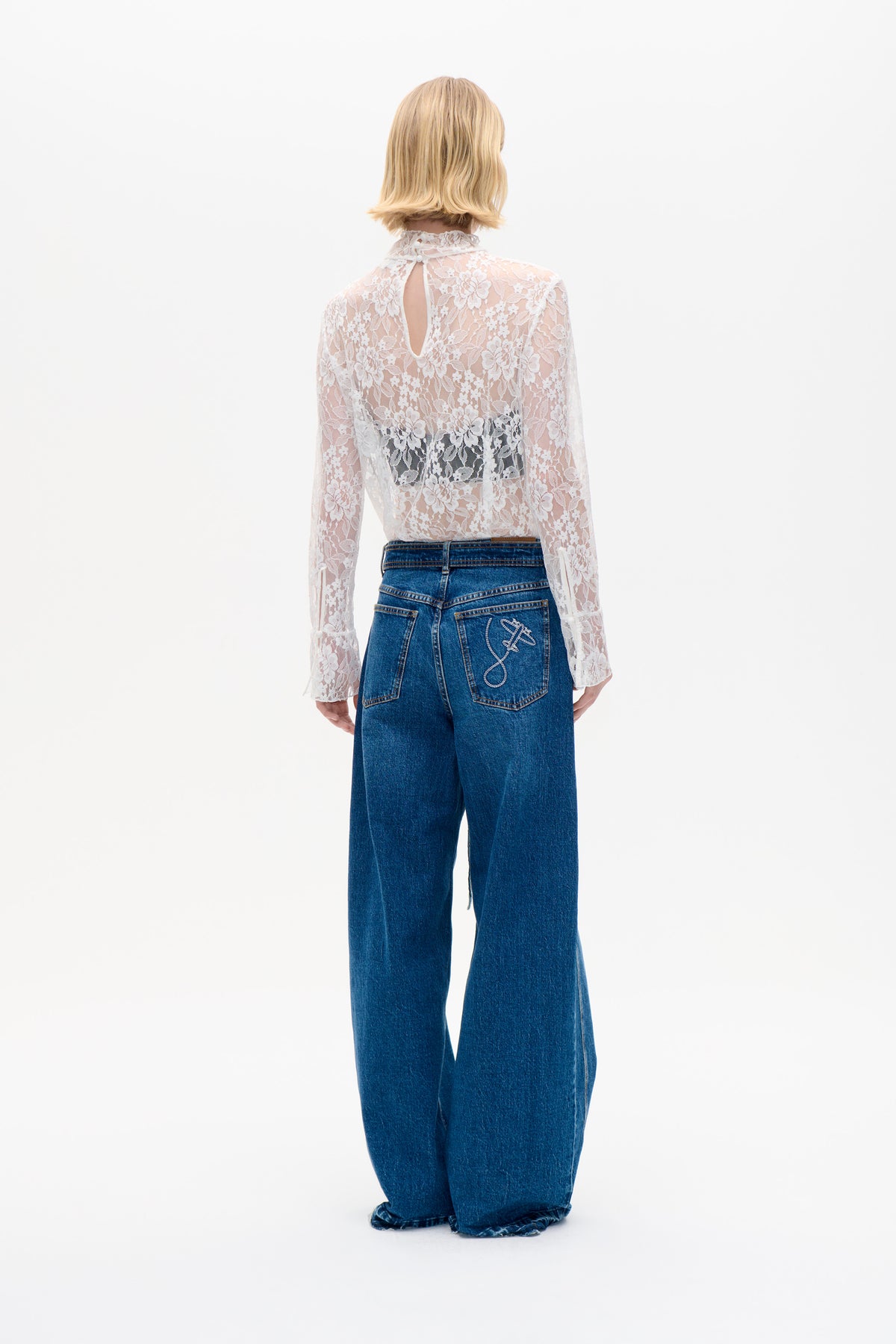Back view of a white floral lace blouse with a high neck and keyhole opening, styled with wide-leg blue jeans.