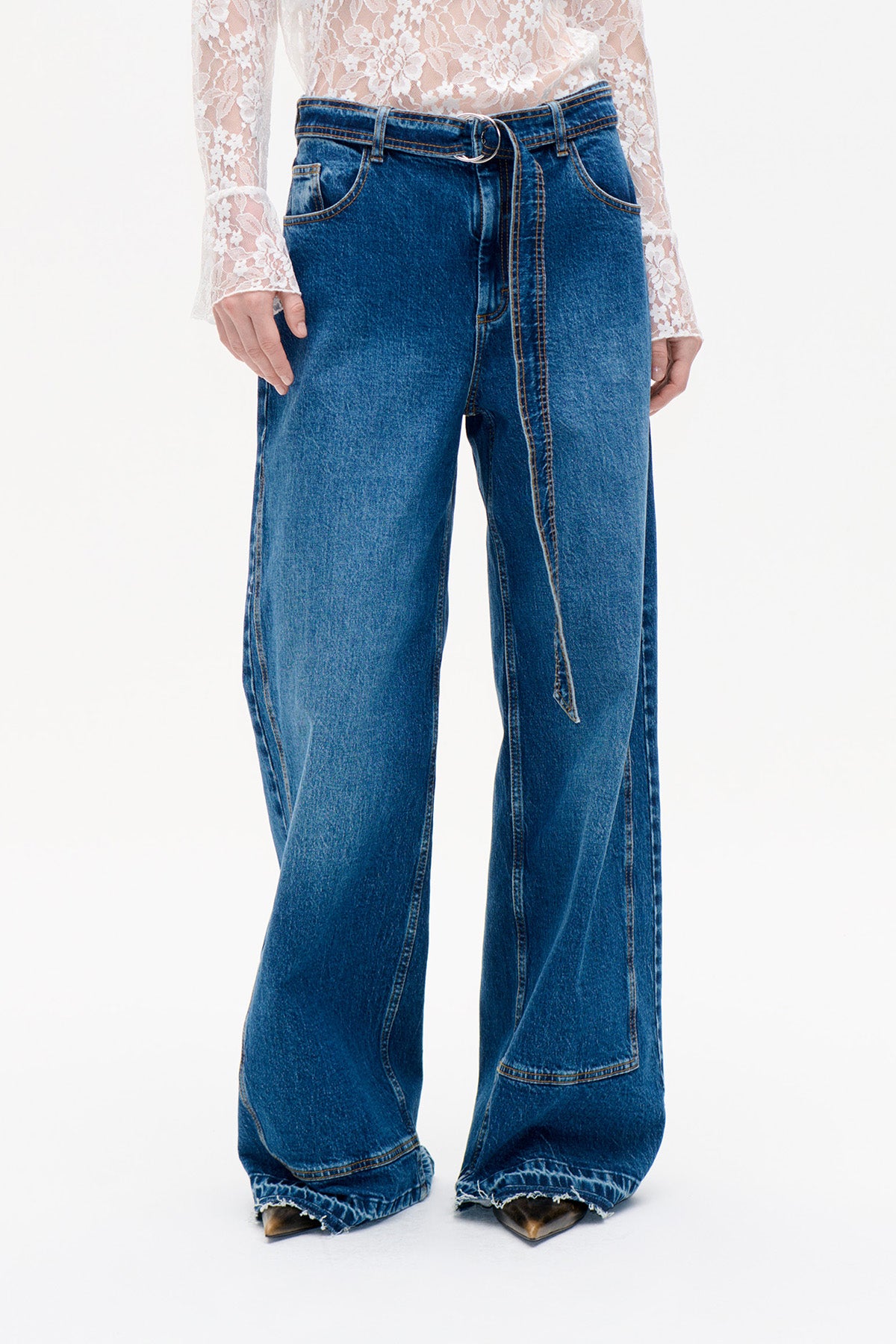Front view of wide-leg blue jeans with a long denim belt and frayed hems, paired with a white floral lace top.