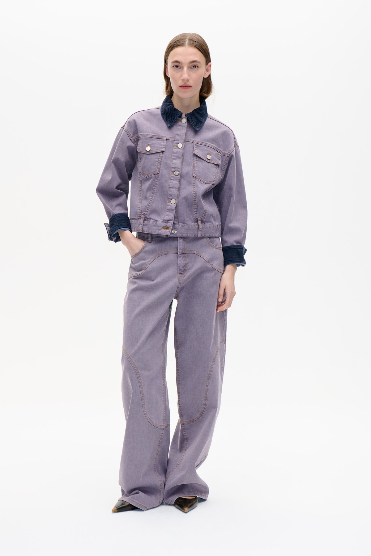 Front view of a model wearing a washed lilac denim jacket with a navy corduroy collar and cuffs, paired with matching wide-leg jeans.
