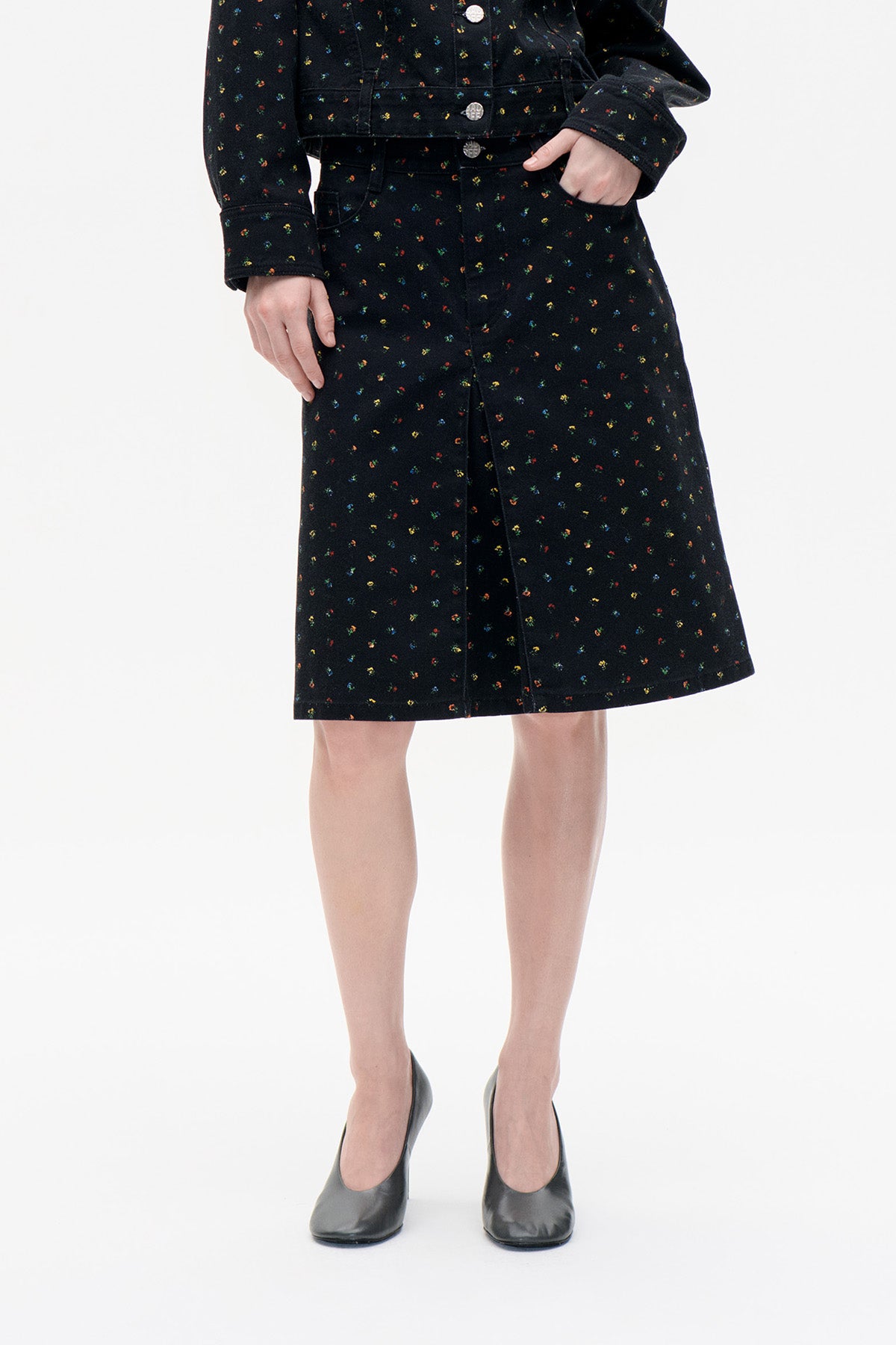 Front view of a black knee-length denim skirt with a front slit and scattered multicoloured floral print, paired with a matching jacket.