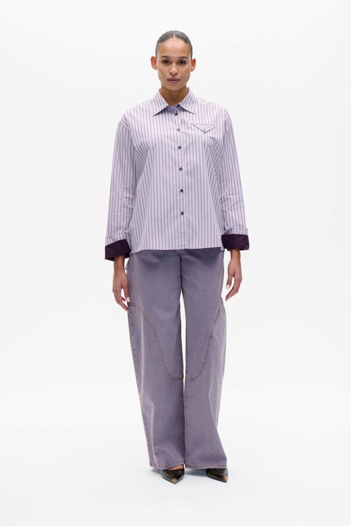 Front view of a model wearing a pale lavender pinstriped shirt with dark cuffs and grey wide-leg trousers.
