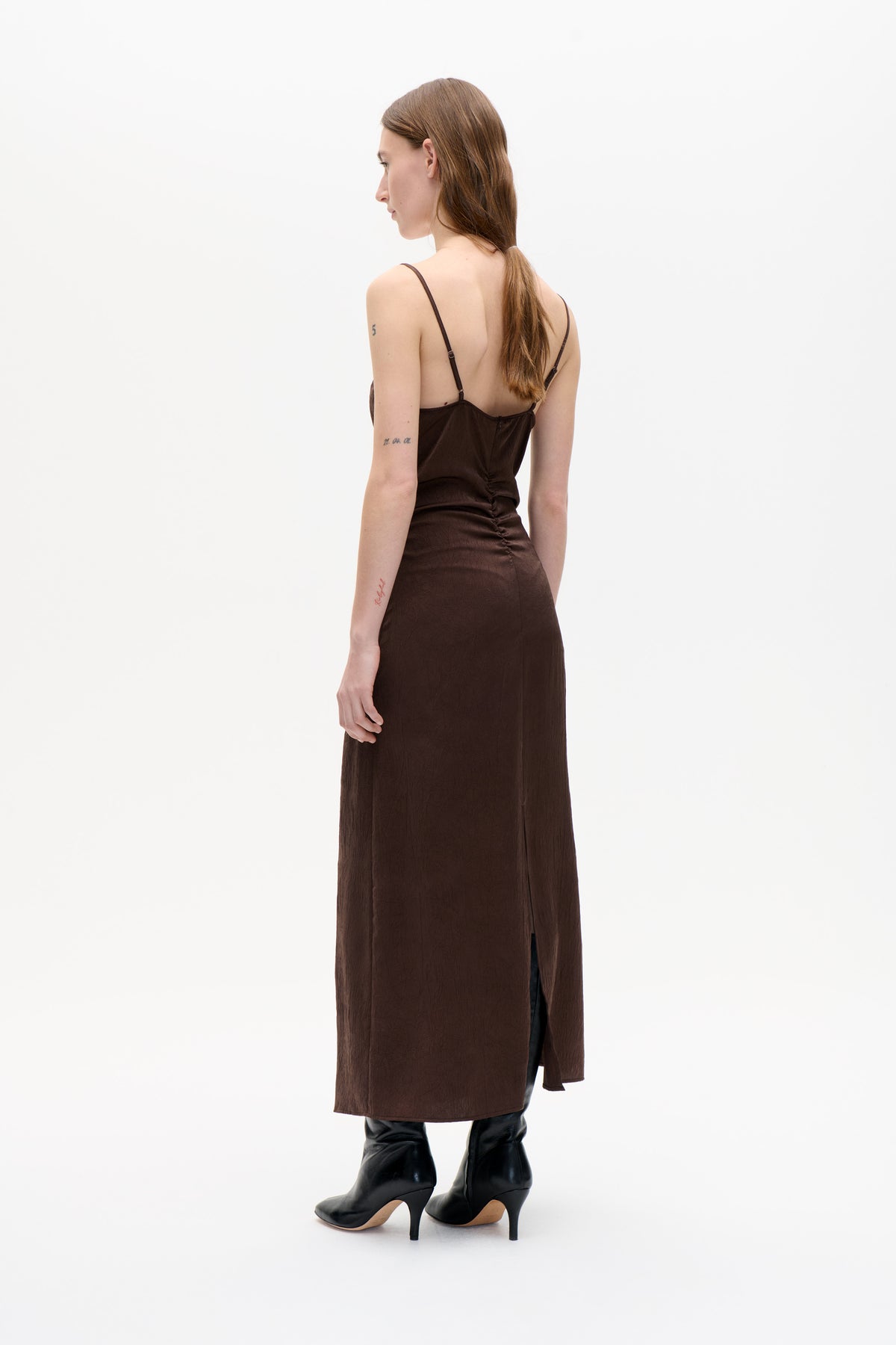 Model wearing a dark brown spaghetti-strap slip dress, shown from the back with a low back and side slit.