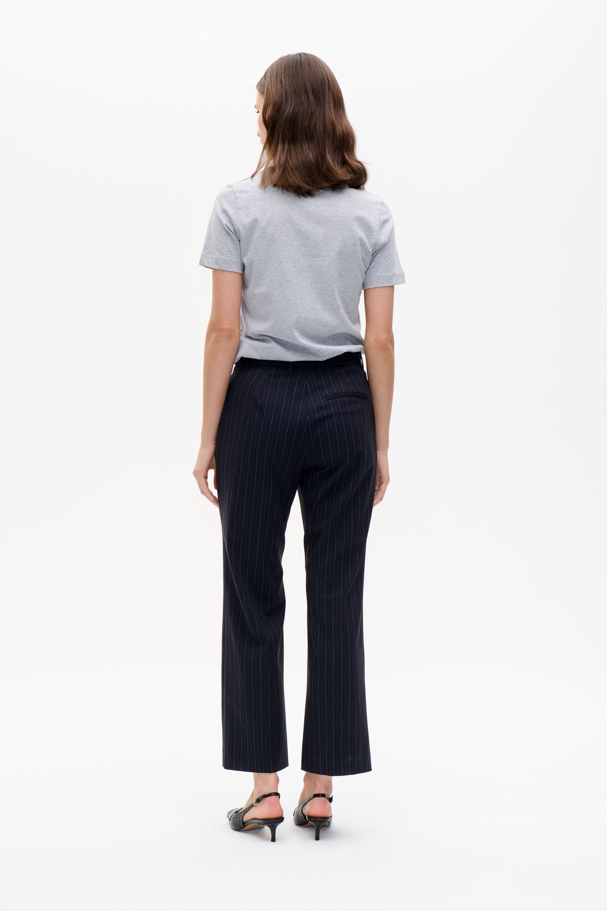 Back view of a model wearing a light grey short-sleeve T-shirt and navy pinstripe cropped trousers with a rear welt pocket.