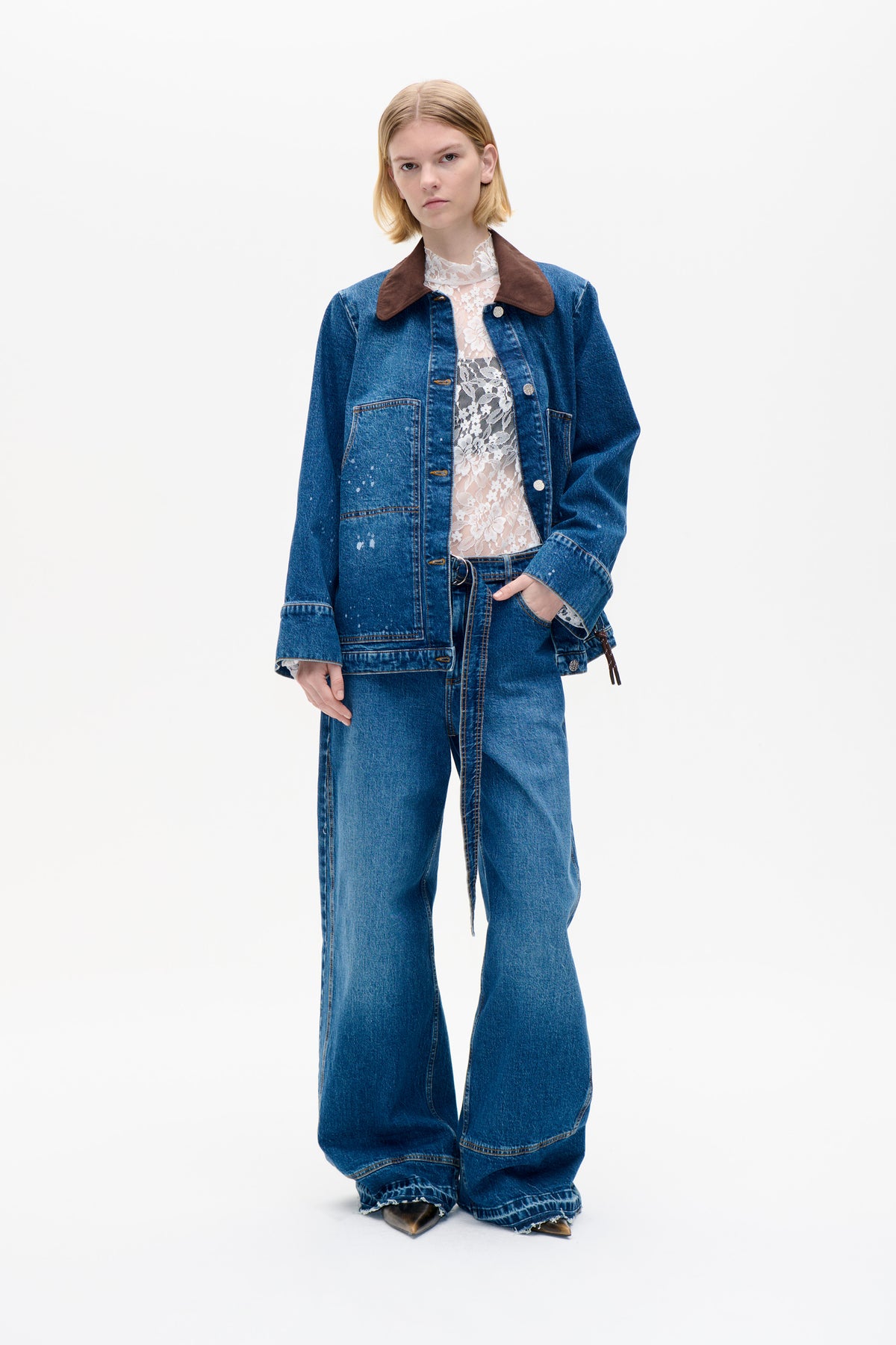 Model wearing a blue denim jacket with a large brown collar over a white floral lace top and matching wide-leg jeans.